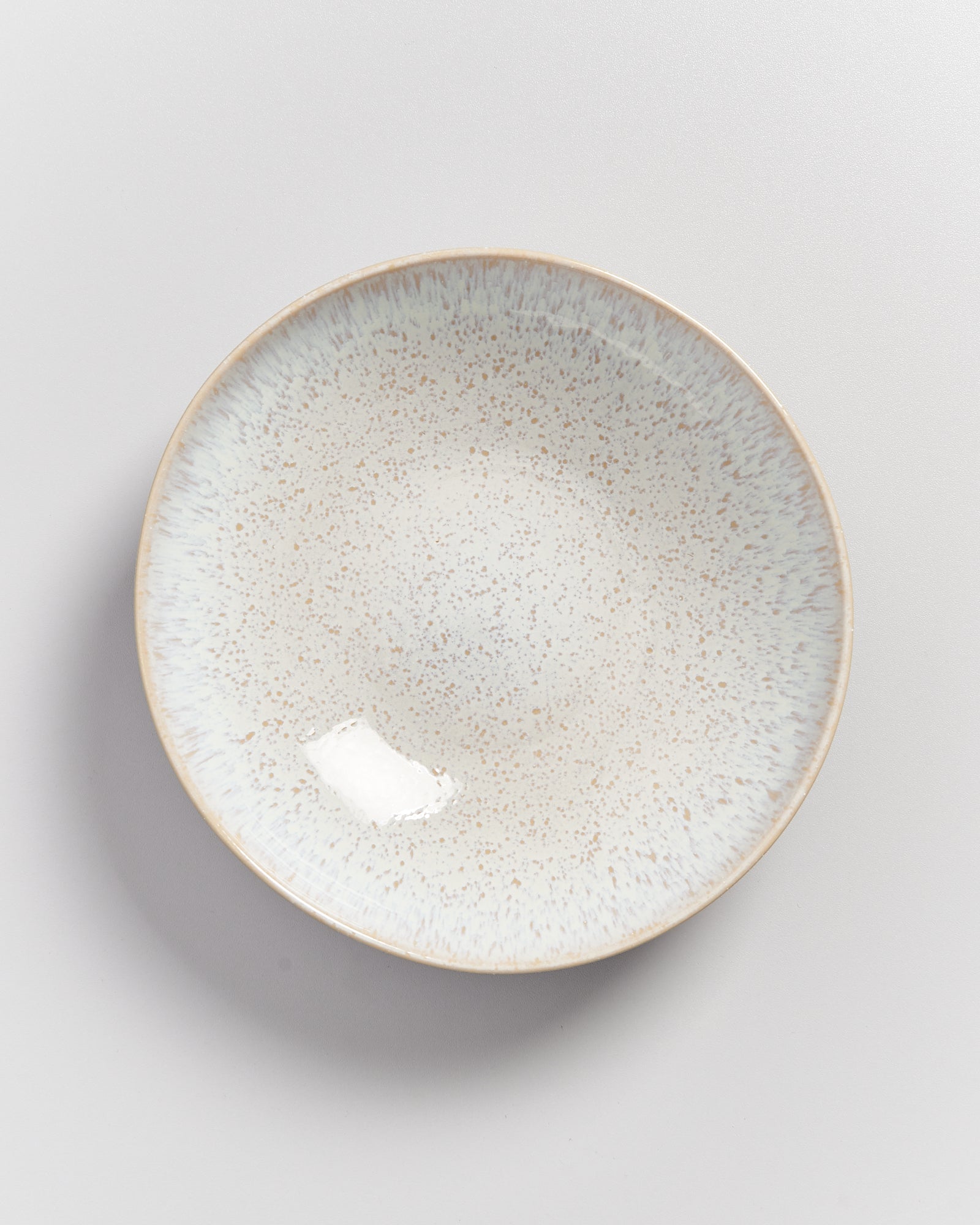 Keramikteller mit gesprenkeltem Muster in Beige- und Blautönen auf weißem Hintergrund.