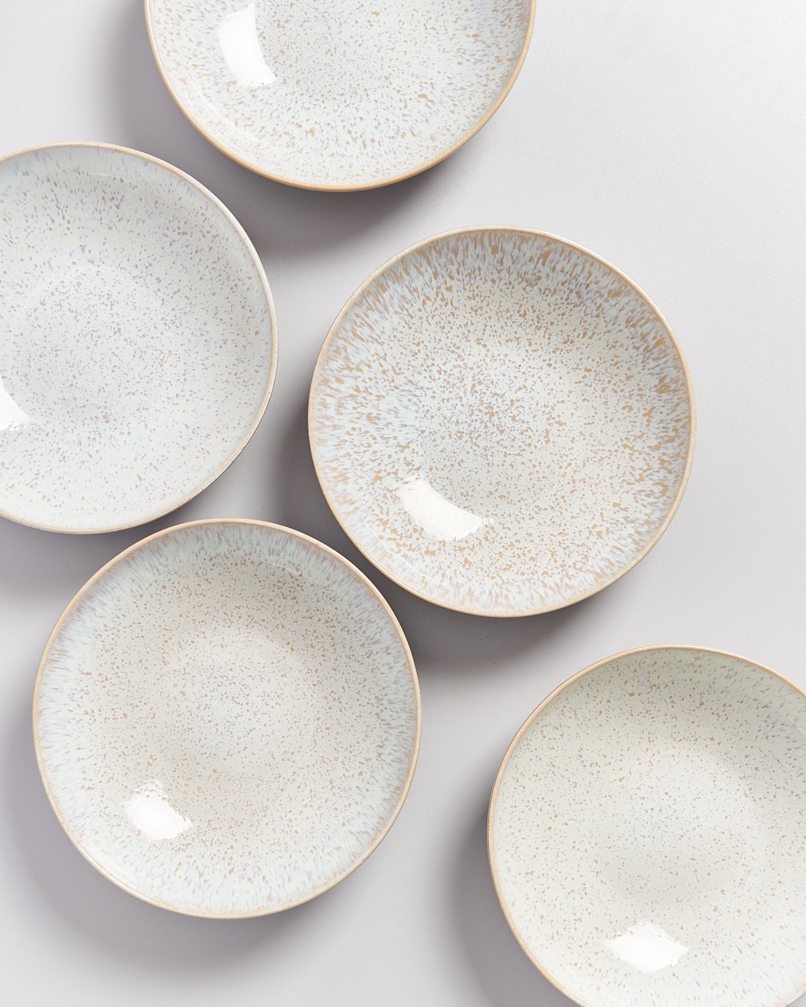 Fünf cremefarbene, gesprenkelte Teller auf einem grauen Hintergrund angeordnet.