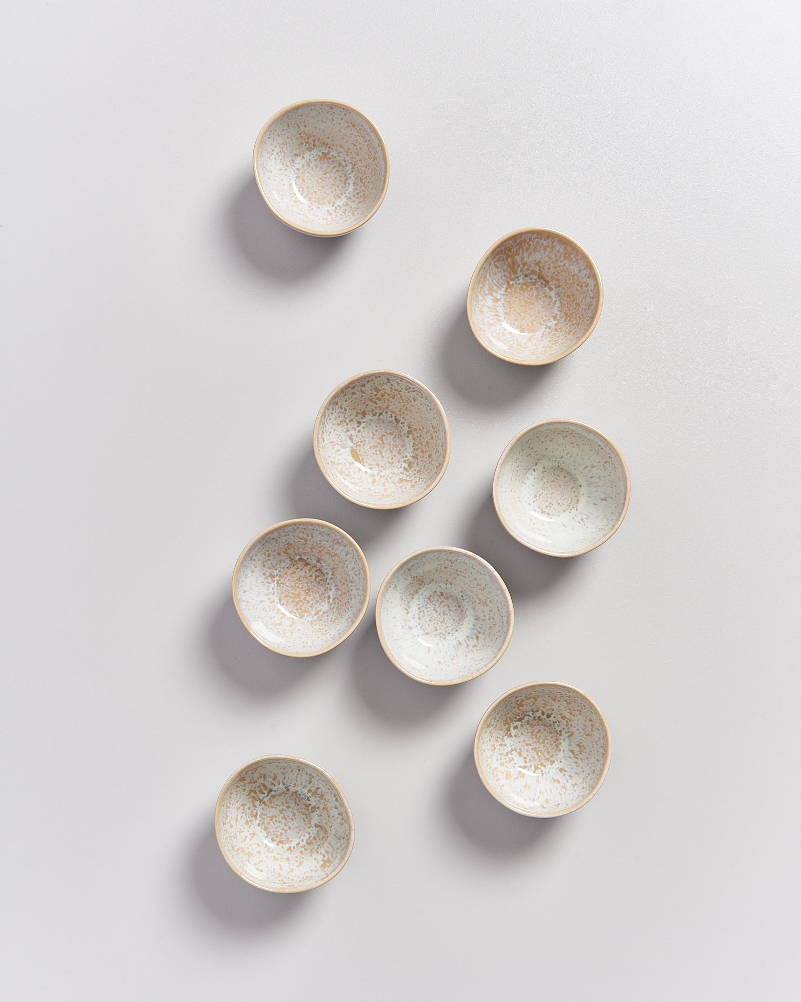 Acht kleine, gepunktete Keramikschalen in zwei Reihen auf einem weißen Hintergrund.