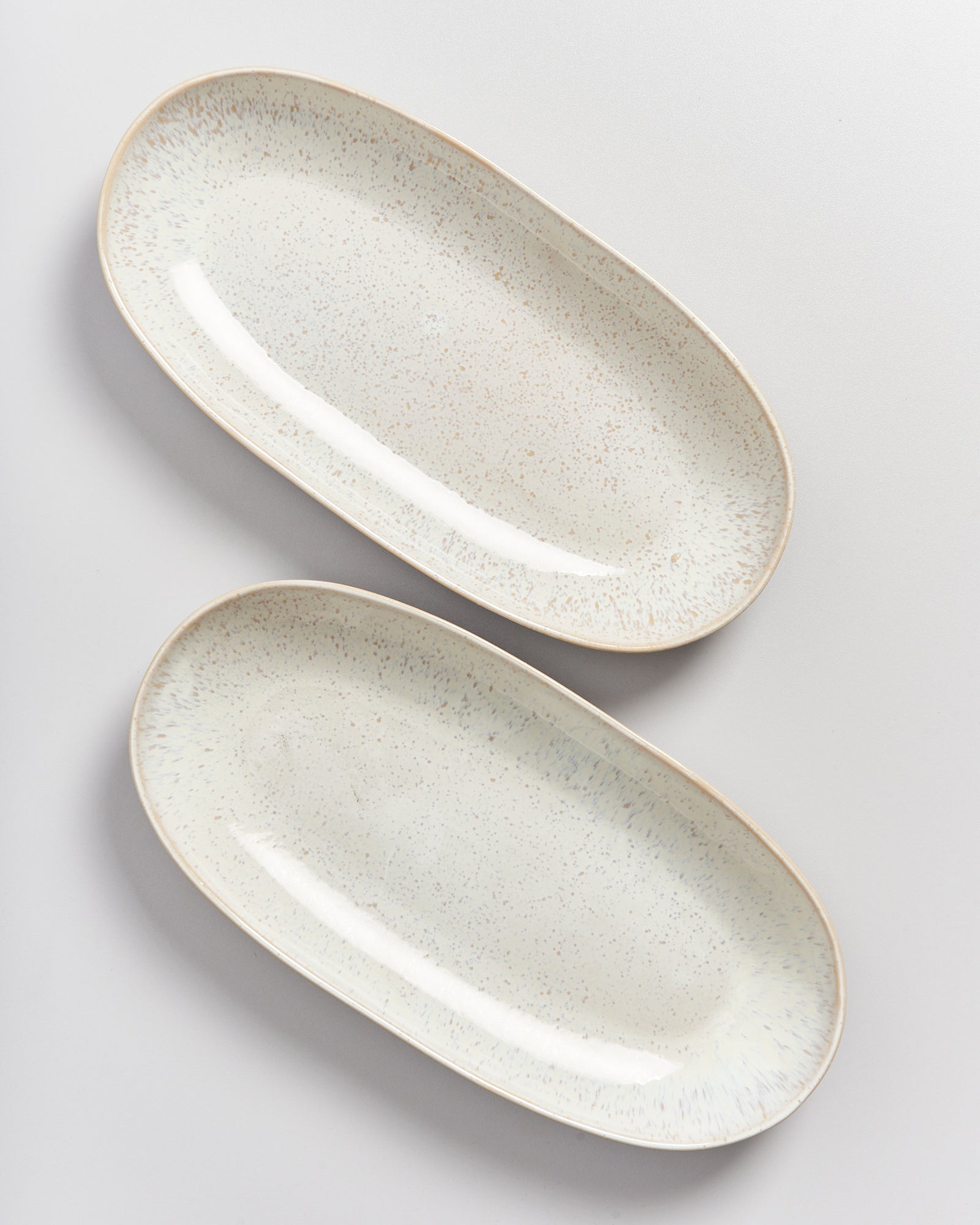Zwei ovale, cremefarbene Servierplatten mit gesprenkeltem Muster auf einer weißen Oberfläche.