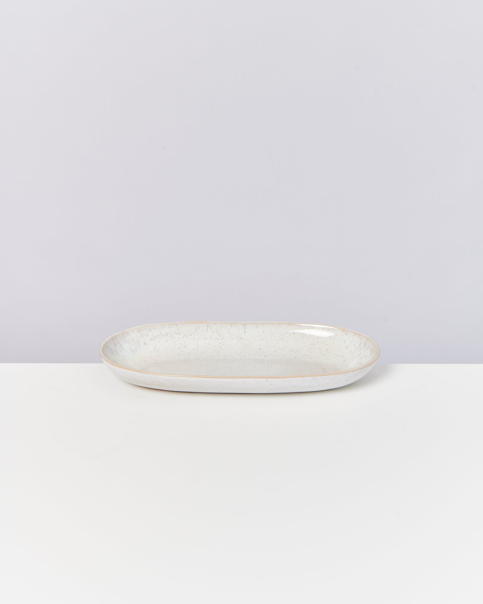 Ovale Keramikplatte mit gesprenkeltem Dekor auf weißem Untergrund.