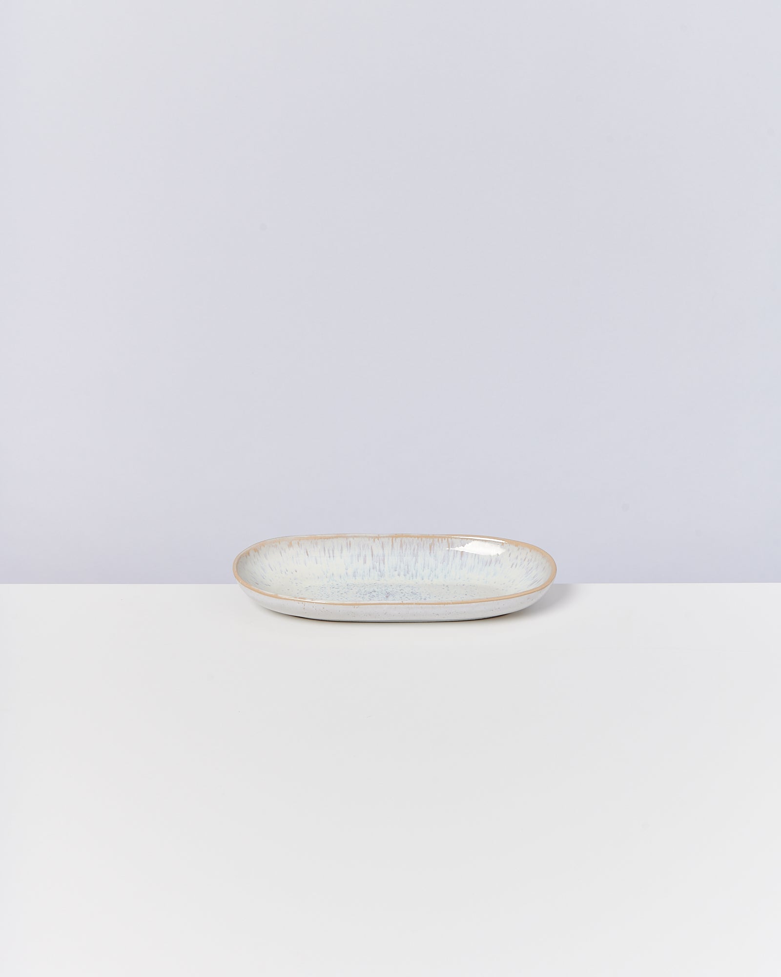 Ein ovaler, flacher Teller mit hellgrüner Glasur steht auf einem weißen Tisch vor einem hellgrauen Hintergrund.