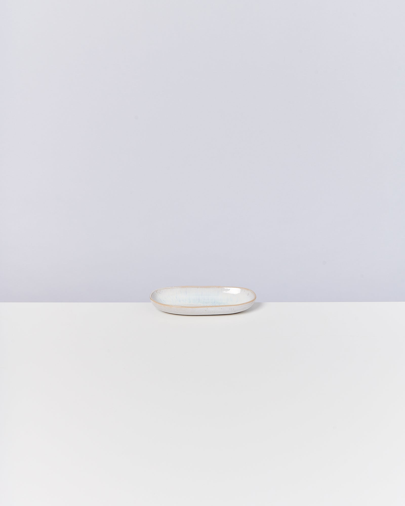 Ein kleines, ovales Keramikschälchen steht auf einem weißen Tisch vor einem schlicht grauen Hintergrund.