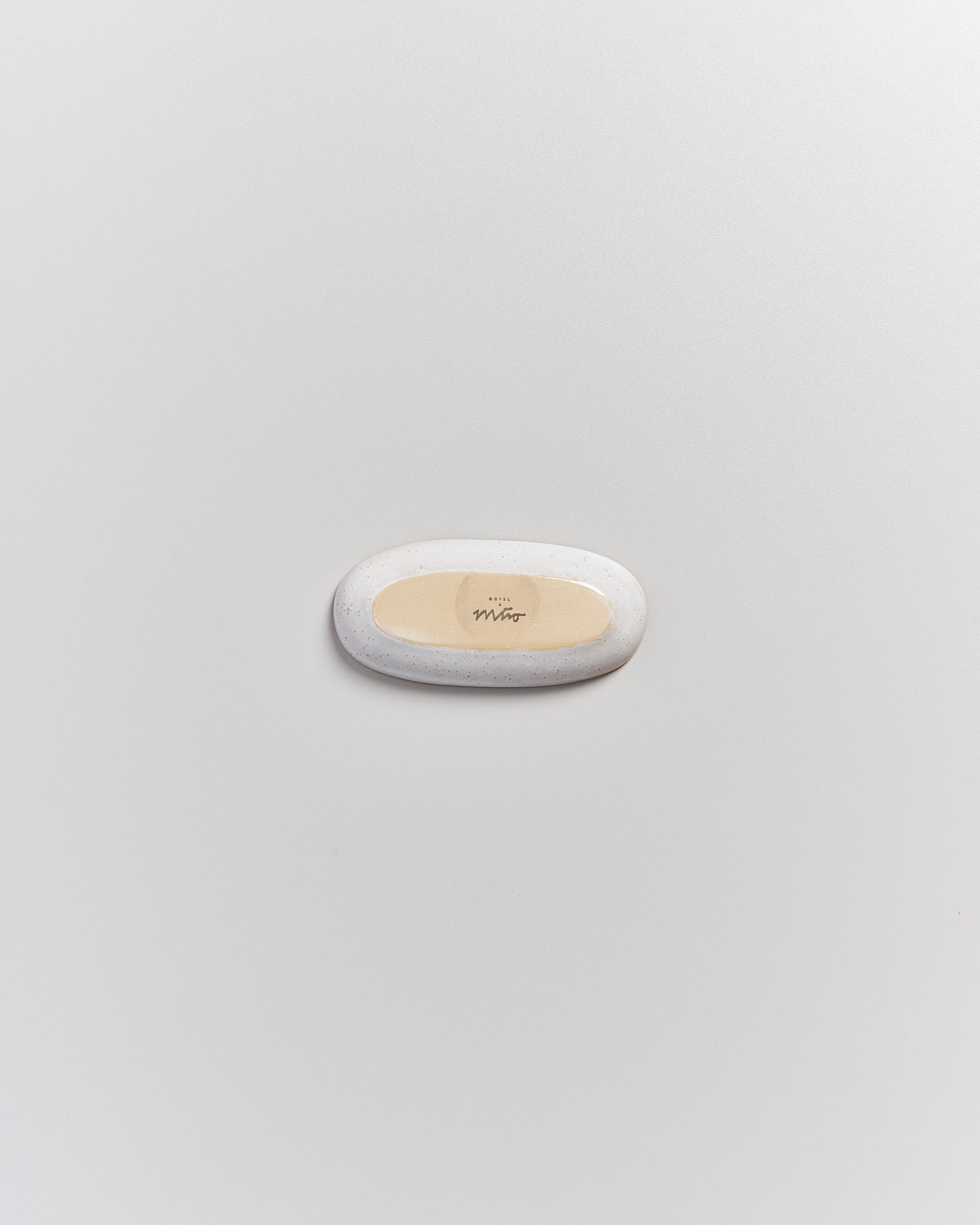 Ovaler Stein mit sandfarbener Vertiefung und Aufschrift auf hellem Hintergrund.