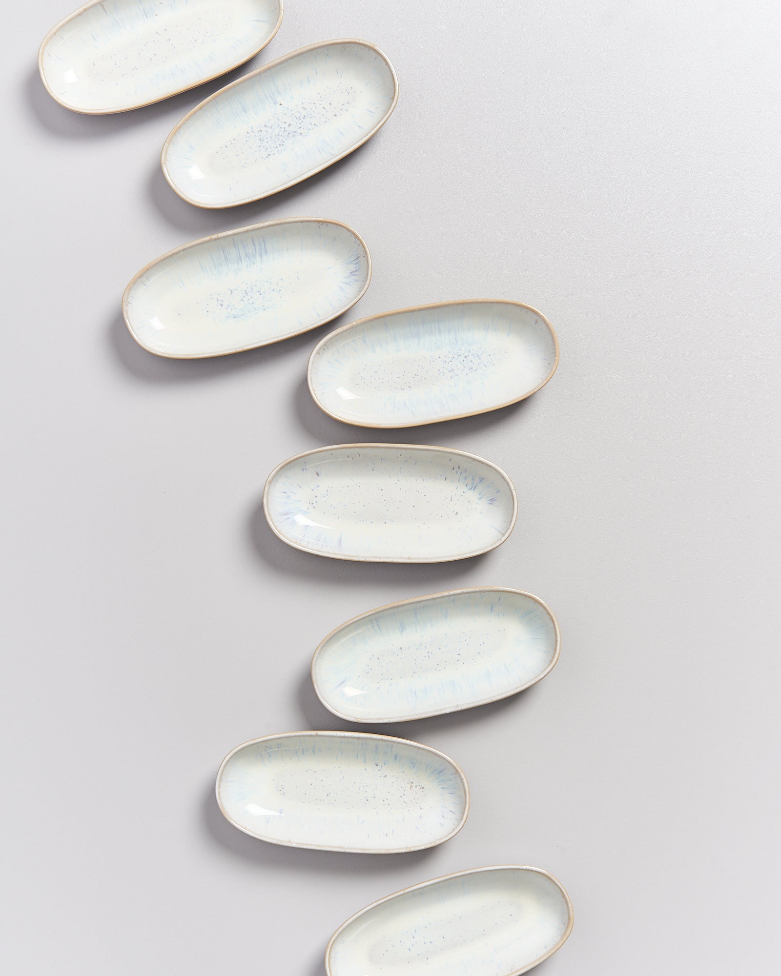 Acht ovale Teller mit hellblauem Muster sind diagonal auf einer grauen Oberfläche angeordnet.