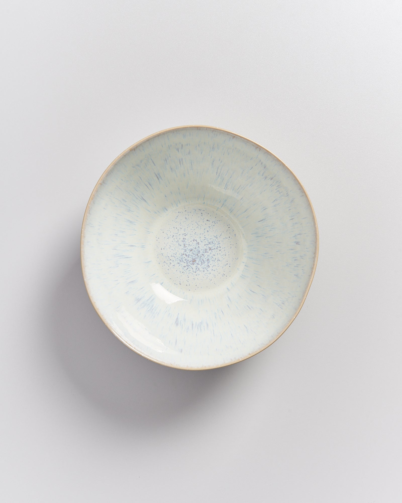 Eine runde, beige Schale mit blauen Sprenkeln auf einem grauen Hintergrund.