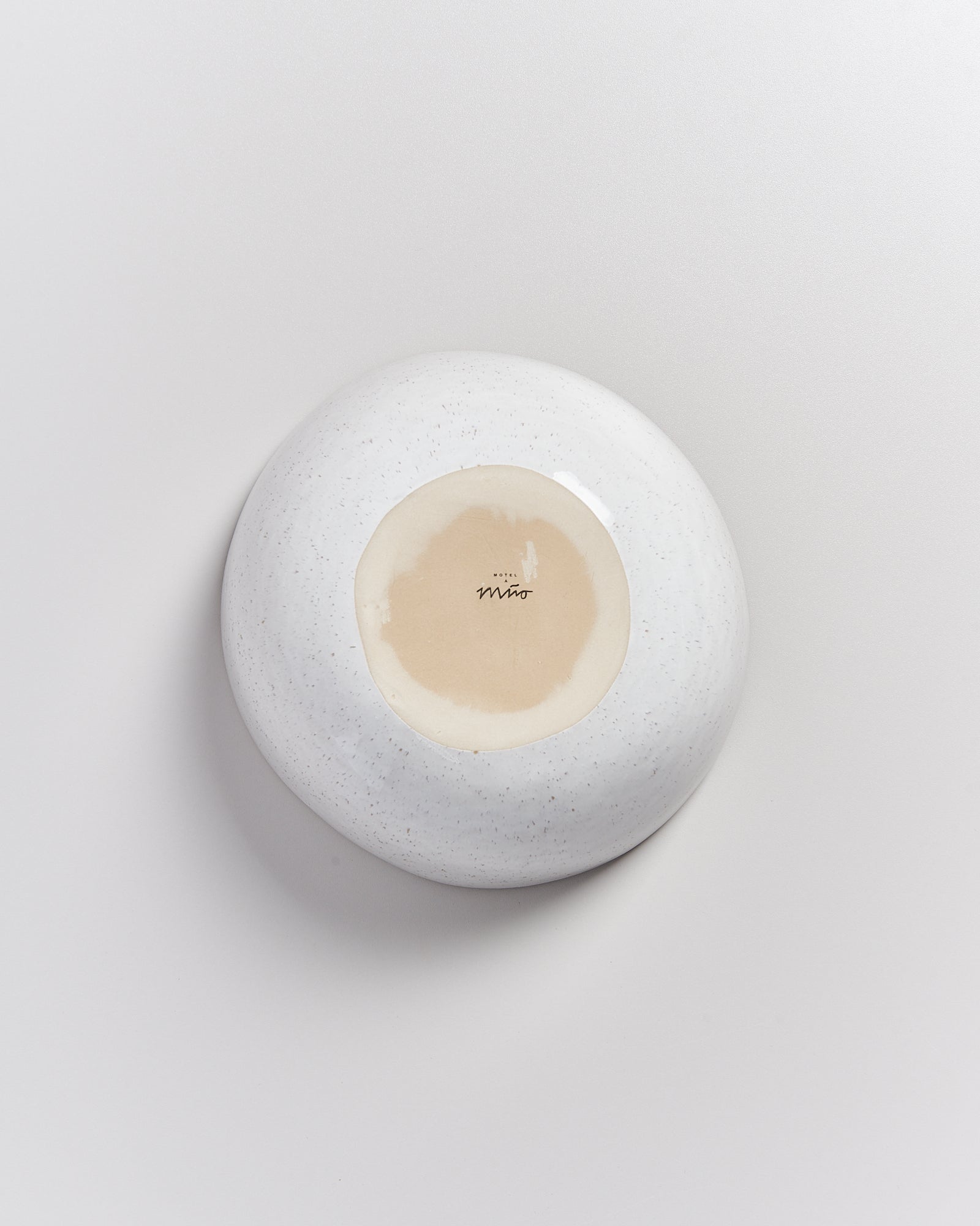 Die Unterseite einer weißen Keramikschale mit einem beigen Kreis und einer Signatur in der Mitte.