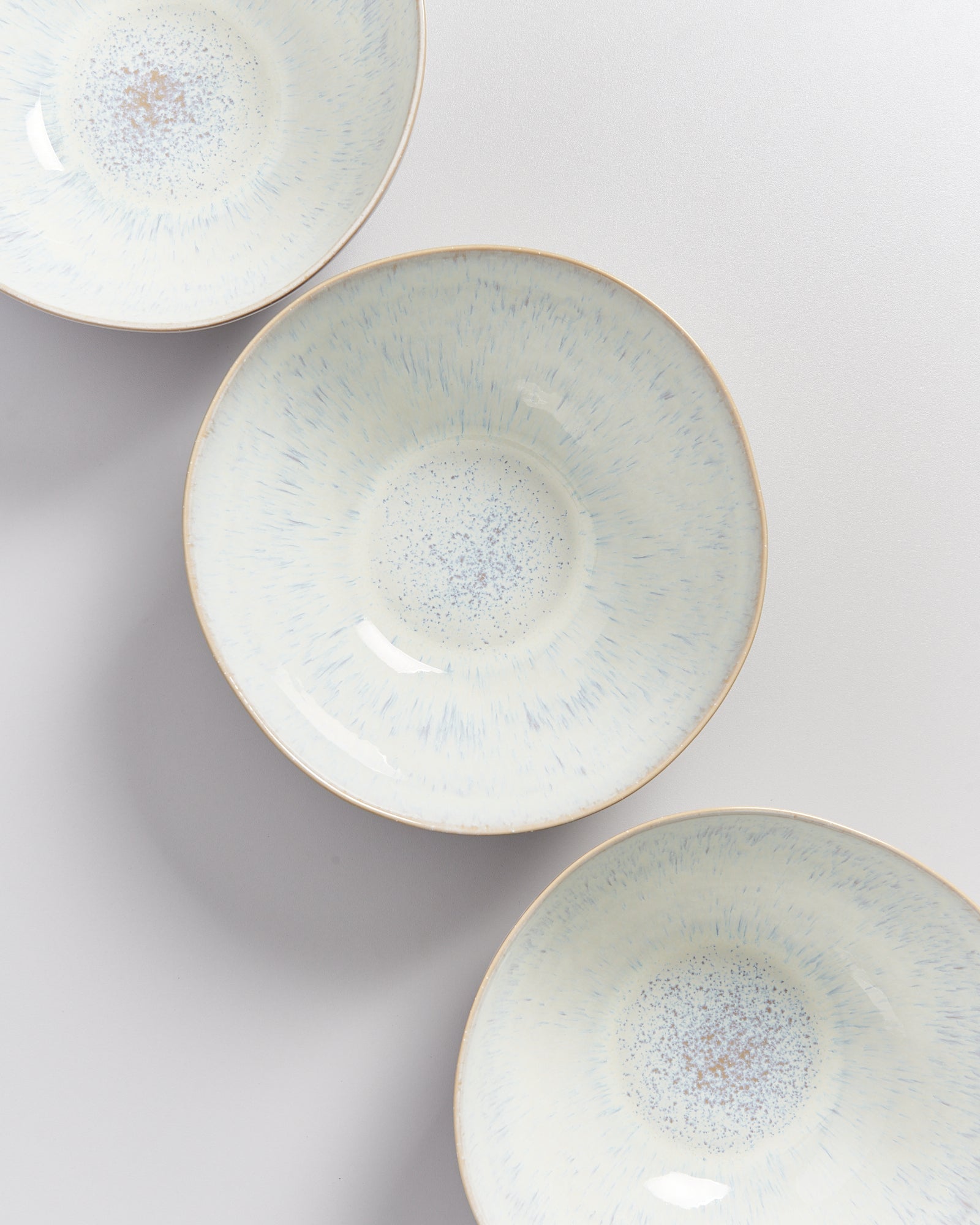 Drei cremefarbene, gesprenkelte Schüsseln mit blauen Akzenten auf grauem Hintergrund.