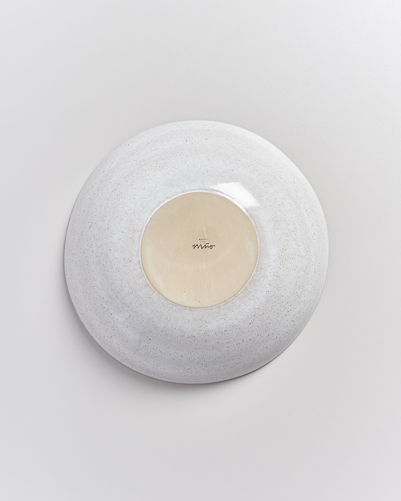 Unterseite eines weißen, gesprenkelten Tellers mit einem kleinen, hellen Kreis in der Mitte auf einem grauen Hintergrund.