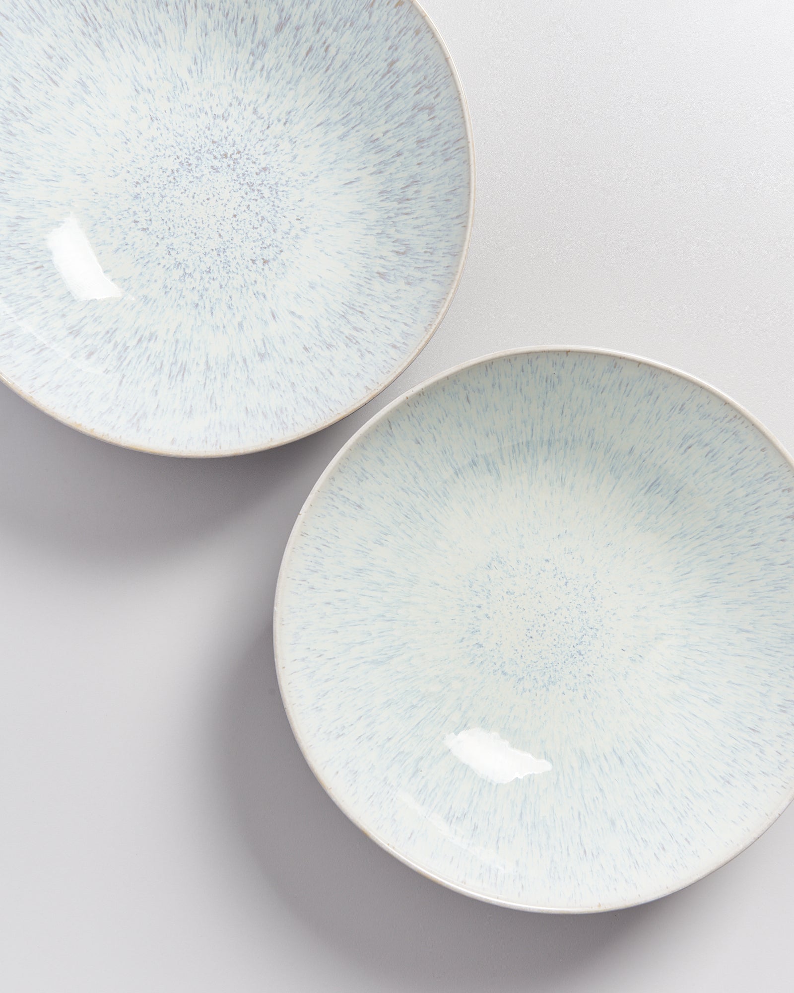 Zwei flache Teller mit einem abstrakten blauen Muster auf hellem Hintergrund.