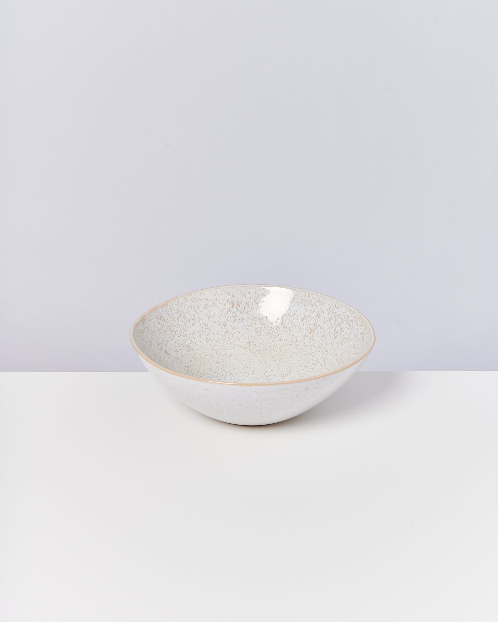 Weiße Schale mit feinen Sprenkeln auf weißem Tisch vor grauem Hintergrund.