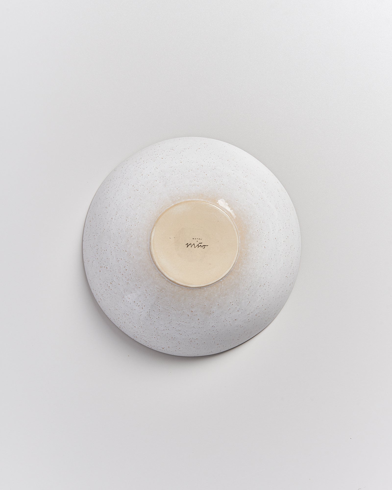 Die Unterseite einer weißen, gesprenkelten Keramikschale mit einer unleserlichen Signatur.