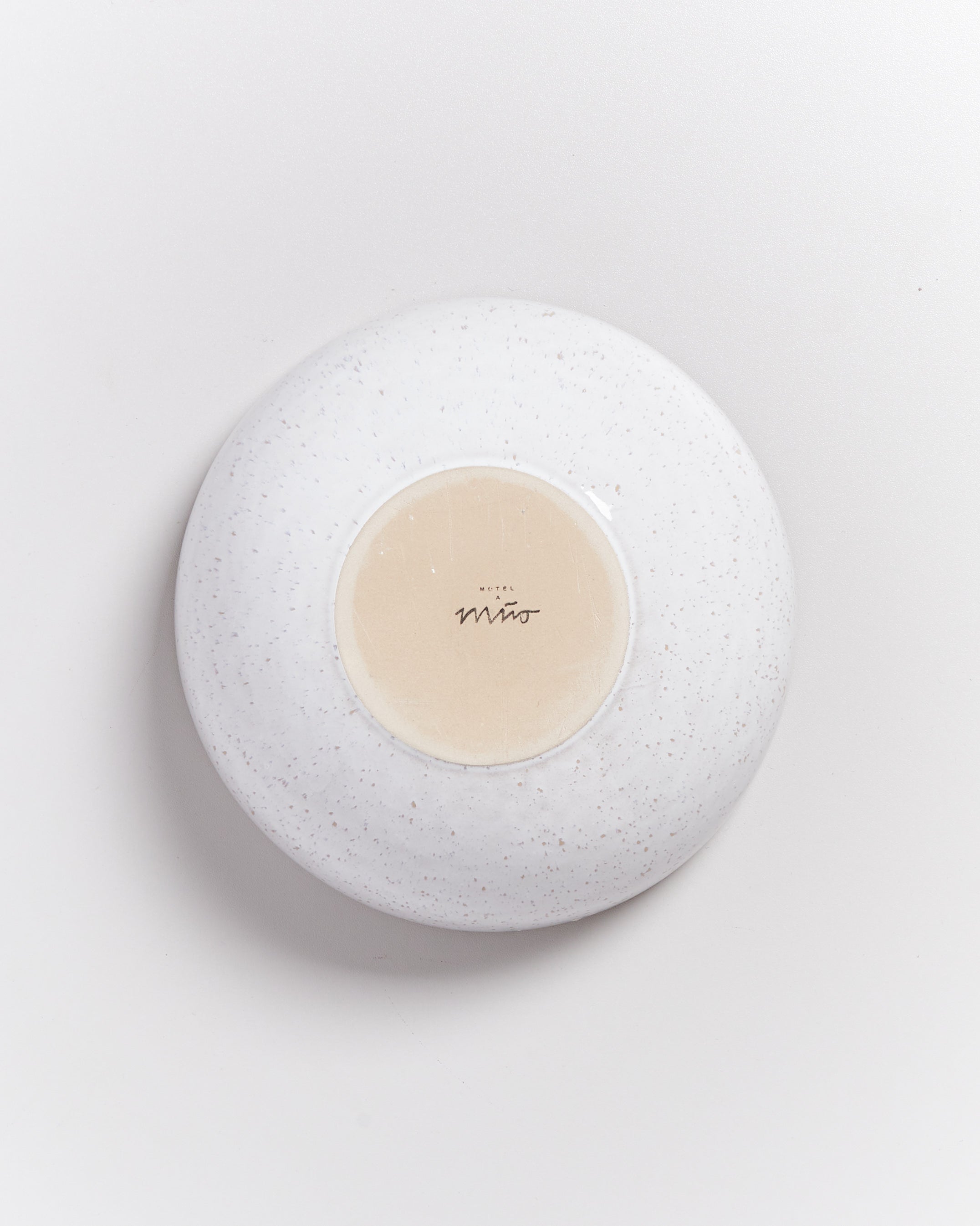 Weiße, flache Schale von unten mit einem cremefarbenen Kreis in der Mitte, auf dem ein Logo steht.
