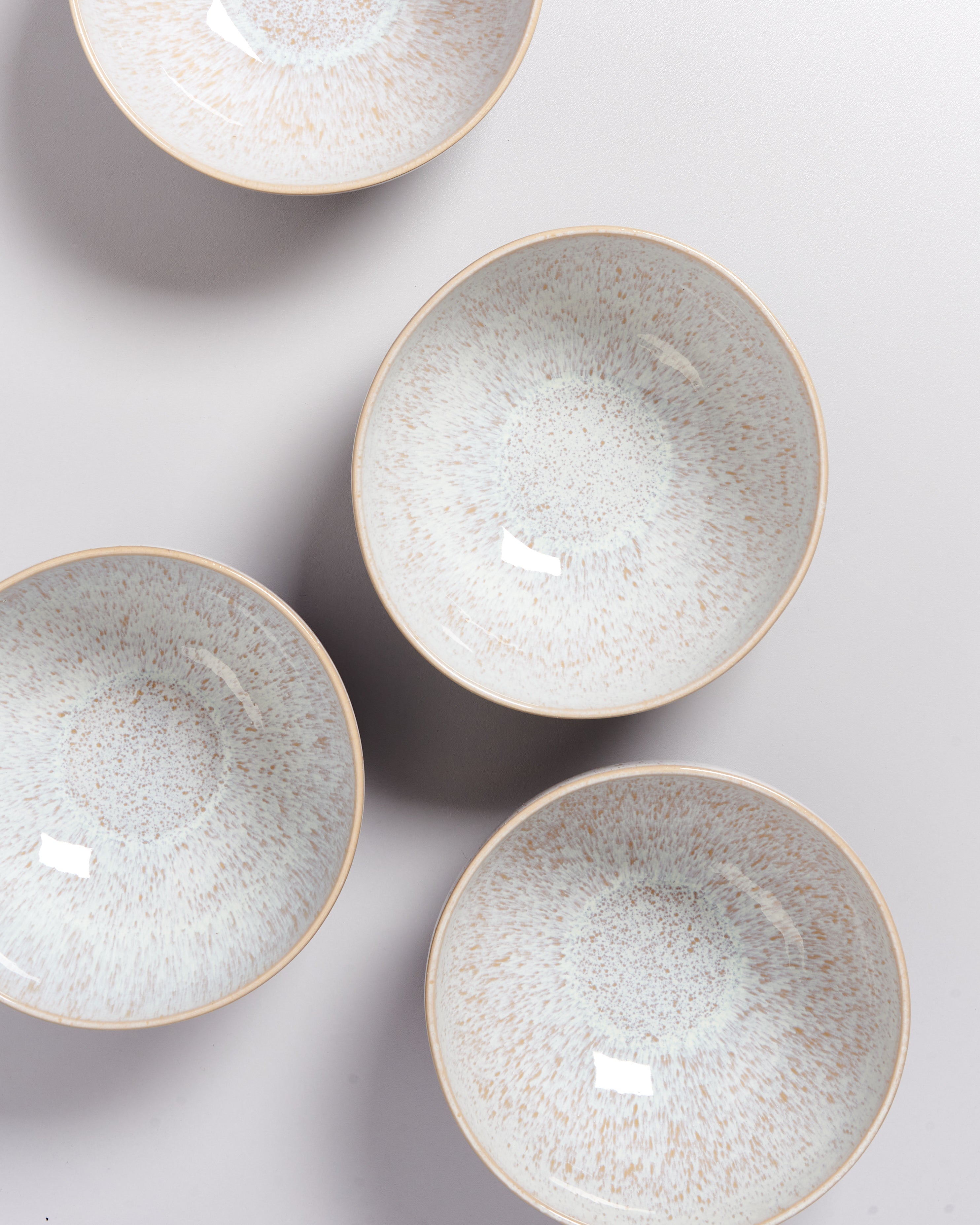 Vier runde, helle, gesprenkelte Schalen mit braunem Rand auf weißem Hintergrund.