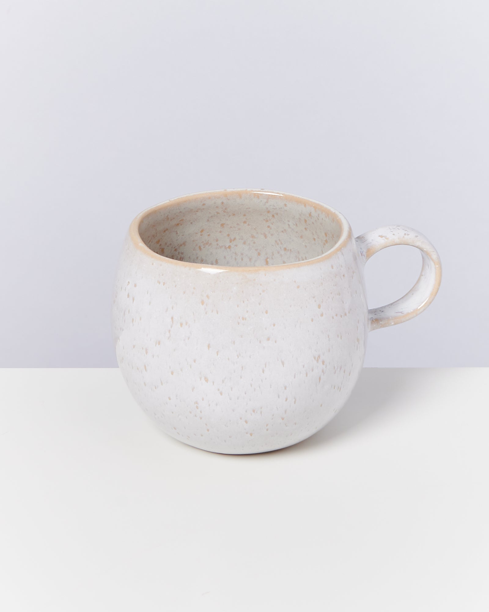 Keramiktasse mit cremefarbenem, gesprenkeltem Design auf weißem Hintergrund.