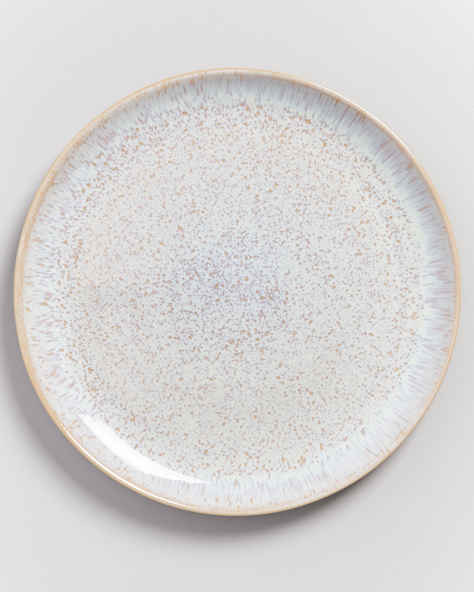 Ein hellgrauer Teller mit gesprenkeltem Muster auf einem weißen Hintergrund.