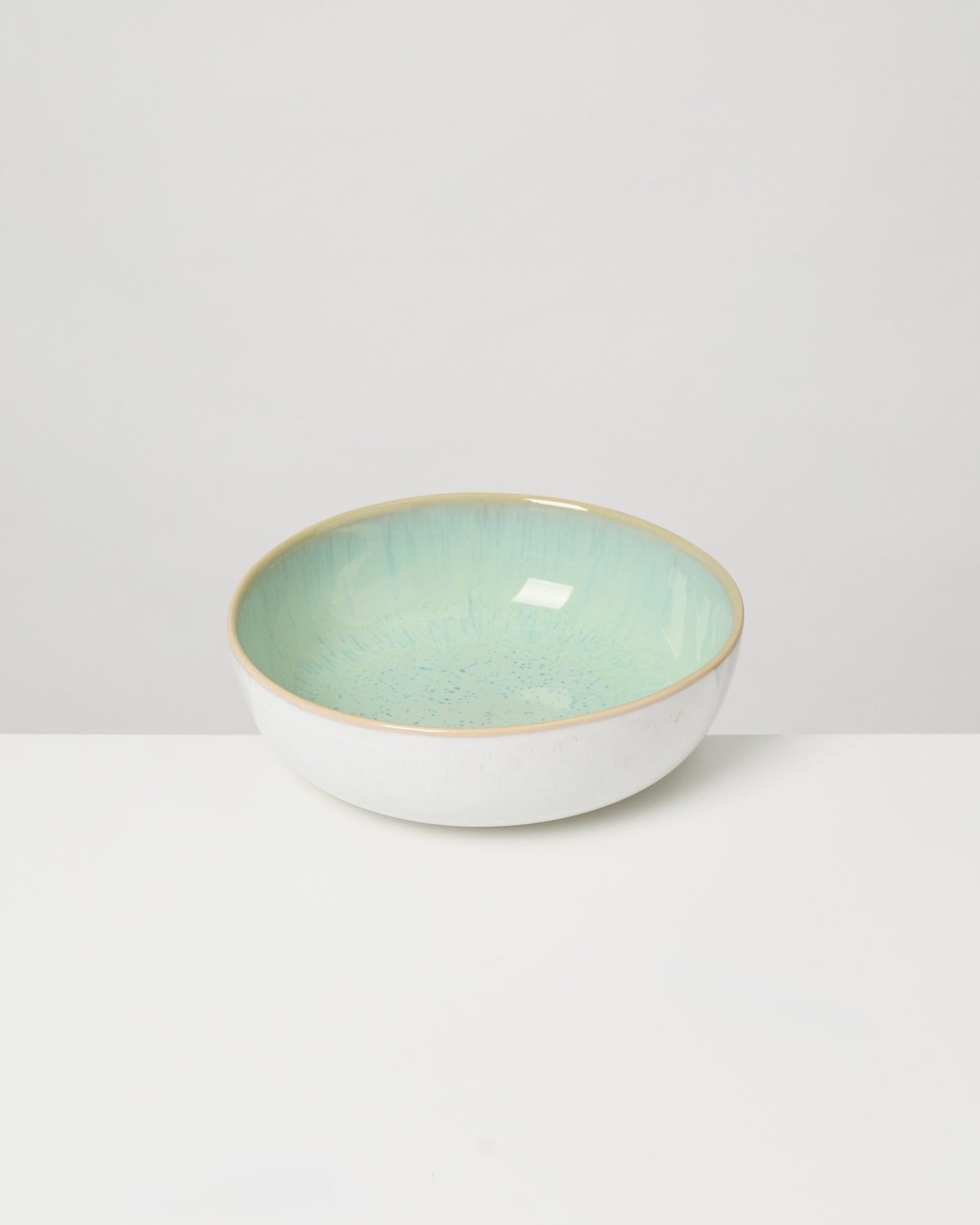 Keramikschüssel mit hellgrüner Innenseite und weißem Äußeren, auf einem weißen Untergrund platziert.
