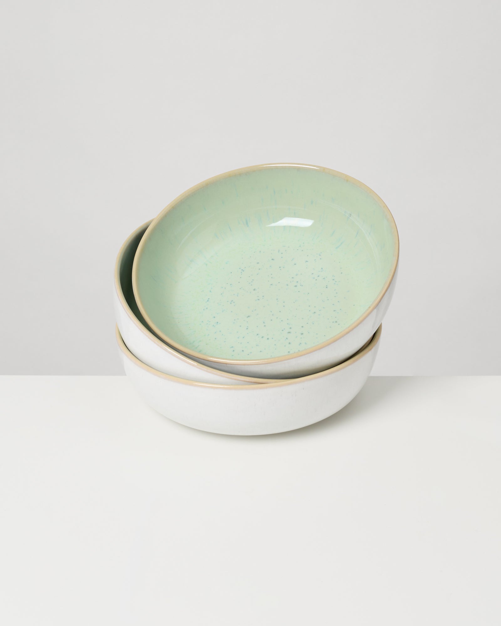 Drei gestapelte, beige Schüsseln mit einem grün gesprenkelten inneren Rand auf einem weißen Hintergrund.