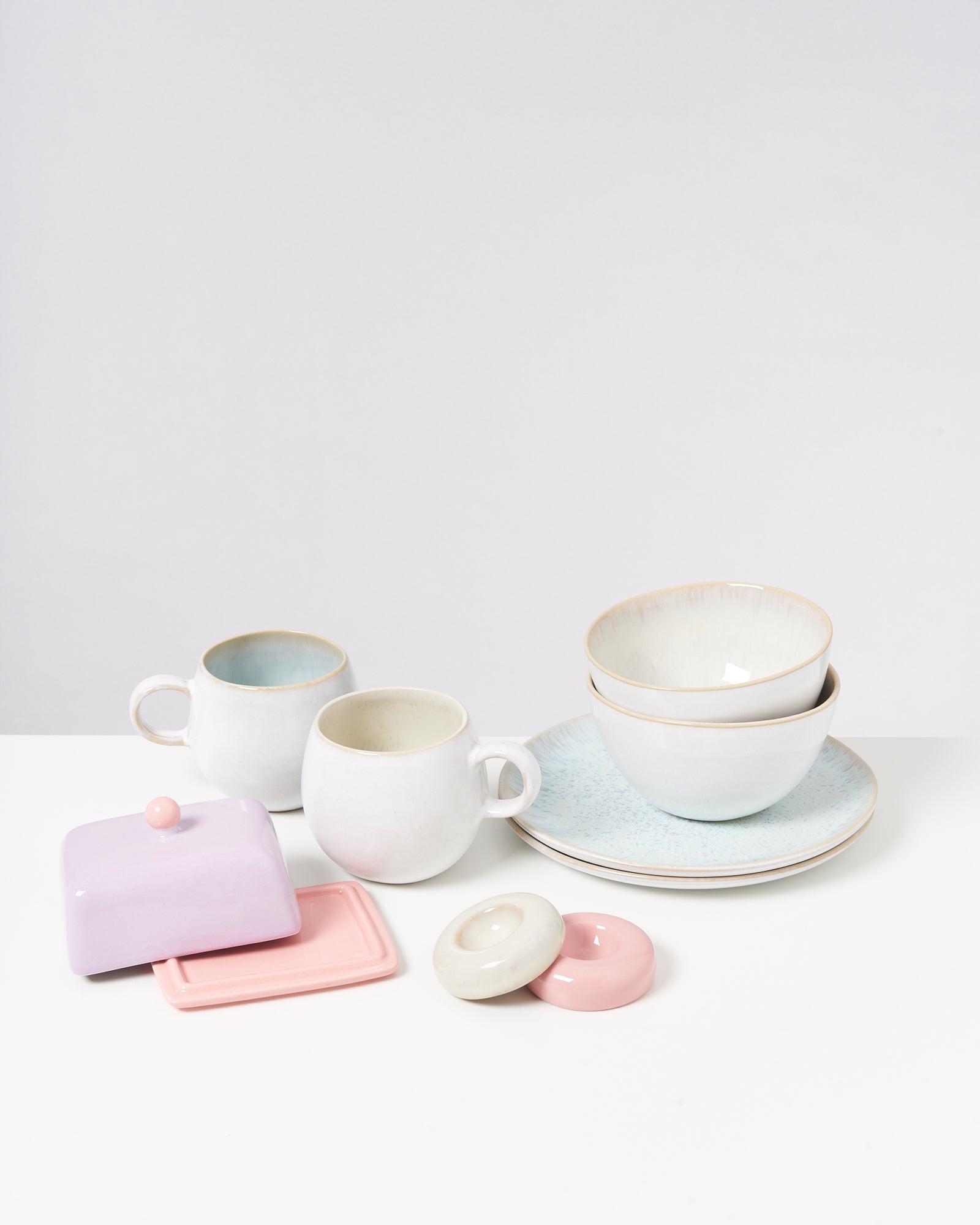 Weißes und pastellfarbenes Geschirr auf einem Tisch, darunter Tassen, Schüsseln, Teller und eine Butterdose.