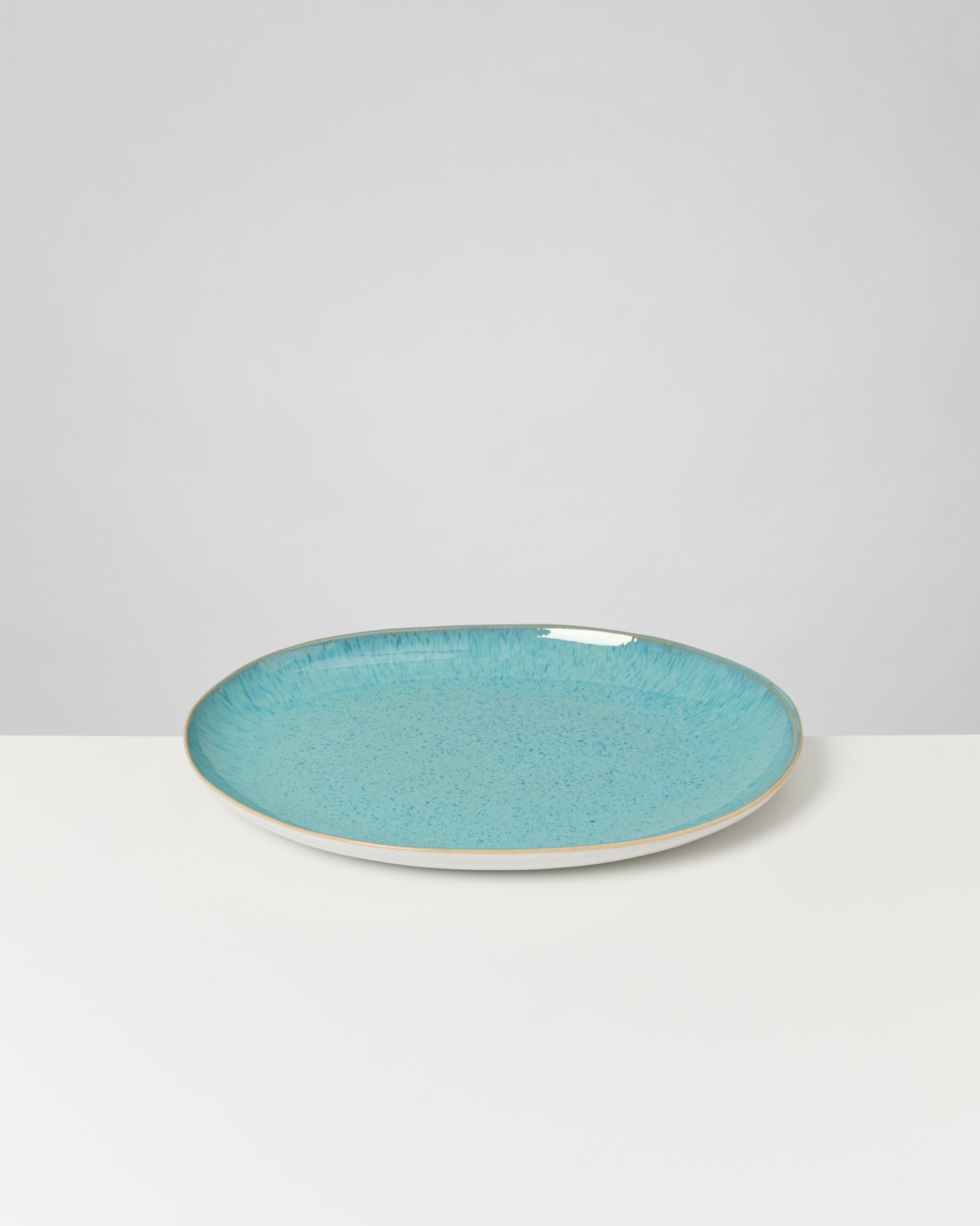 Ein blauer, flacher Teller mit einem Muster liegt auf einer weißen Oberfläche vor grauem Hintergrund.