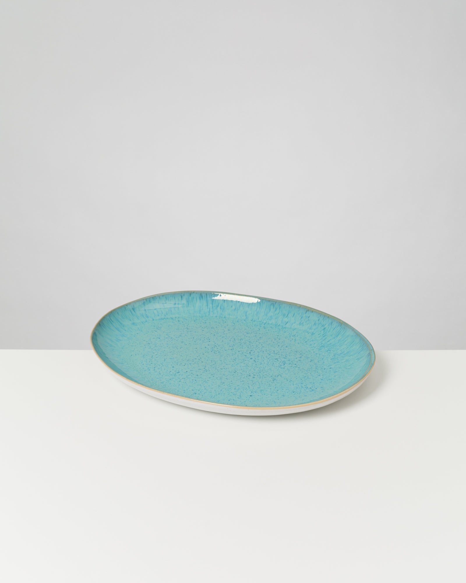 Ein ovaler, hellblauer Keramikteller mit leicht erhöhtem Rand auf weißem Hintergrund.