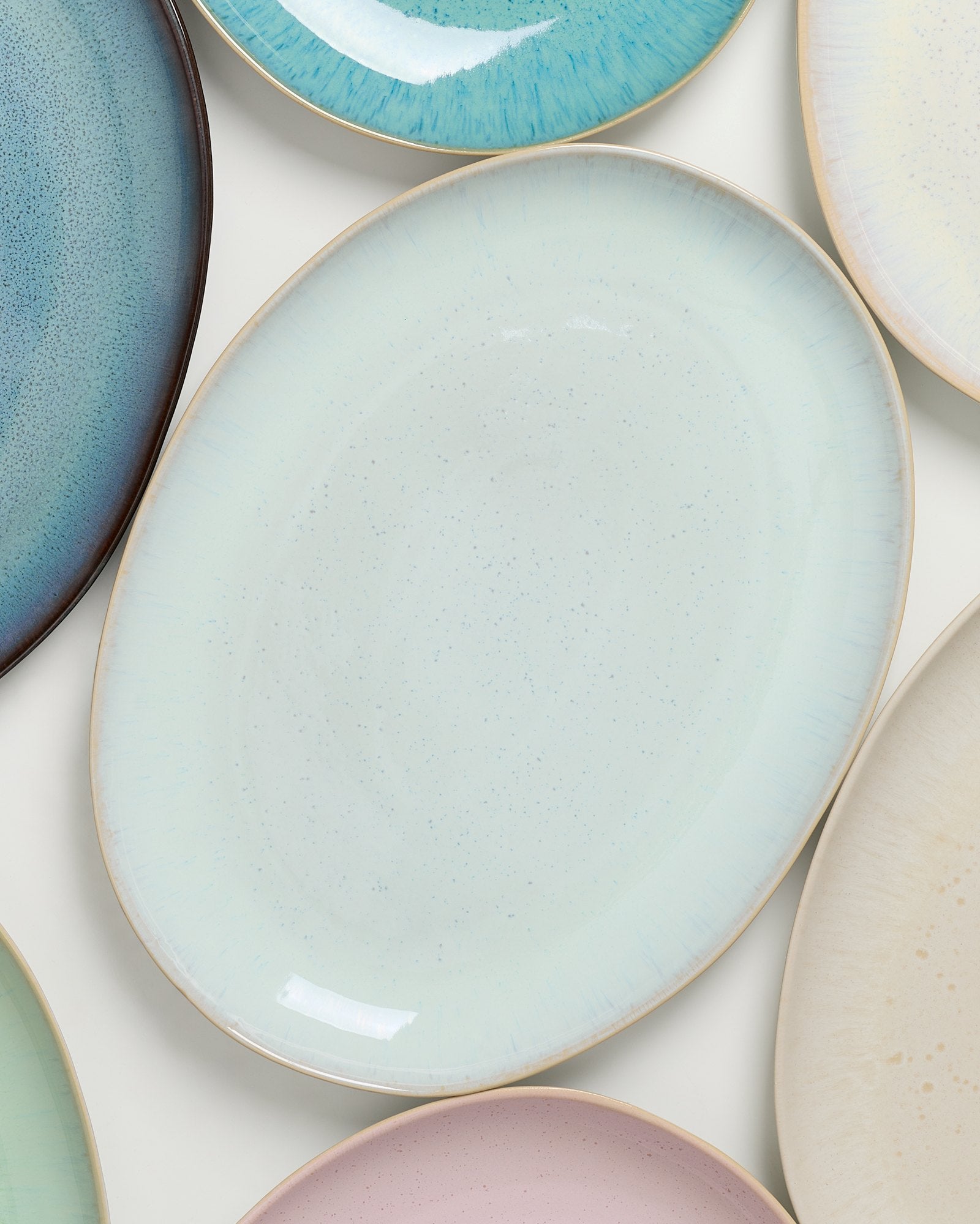 Verschiedene ovale, bunte Teller mit gesprenkelten Mustern liegen nebeneinander.