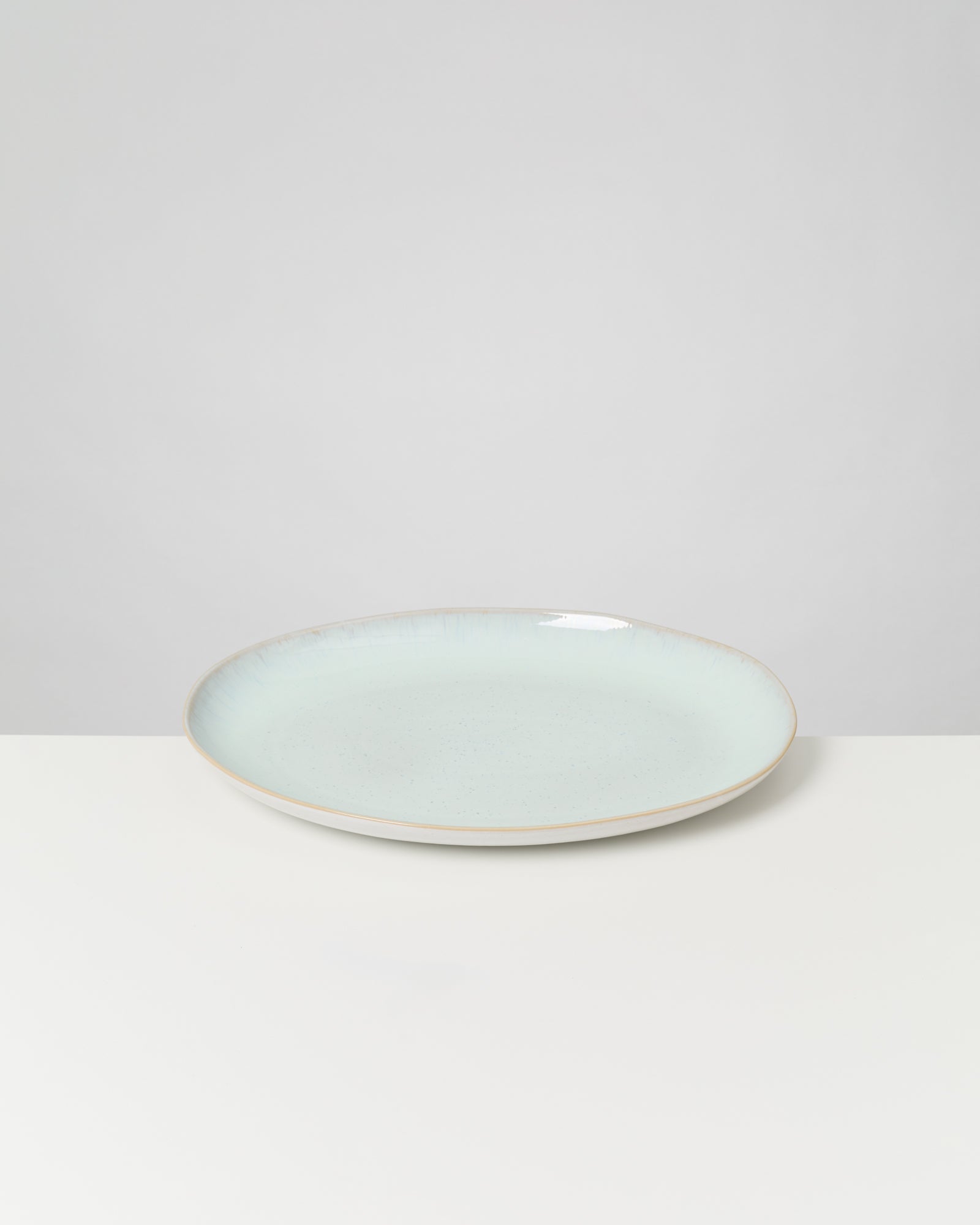 Ein hellblauer Keramikteller steht auf einer weißen Oberfläche vor einem grauen Hintergrund.