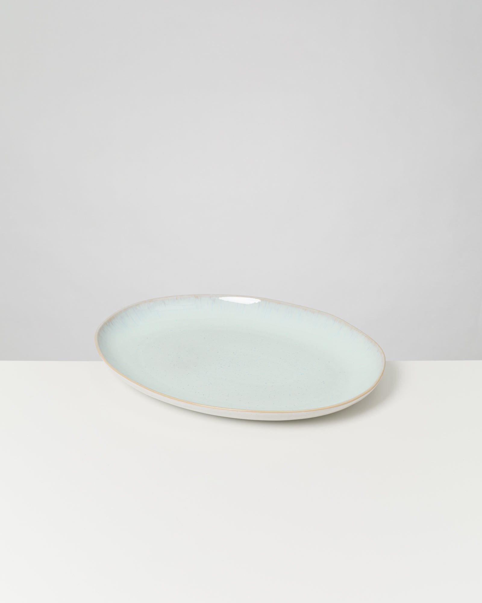 Ein hellblauer, ovaler Teller auf einem weißen Tisch vor einem neutralen Hintergrund.