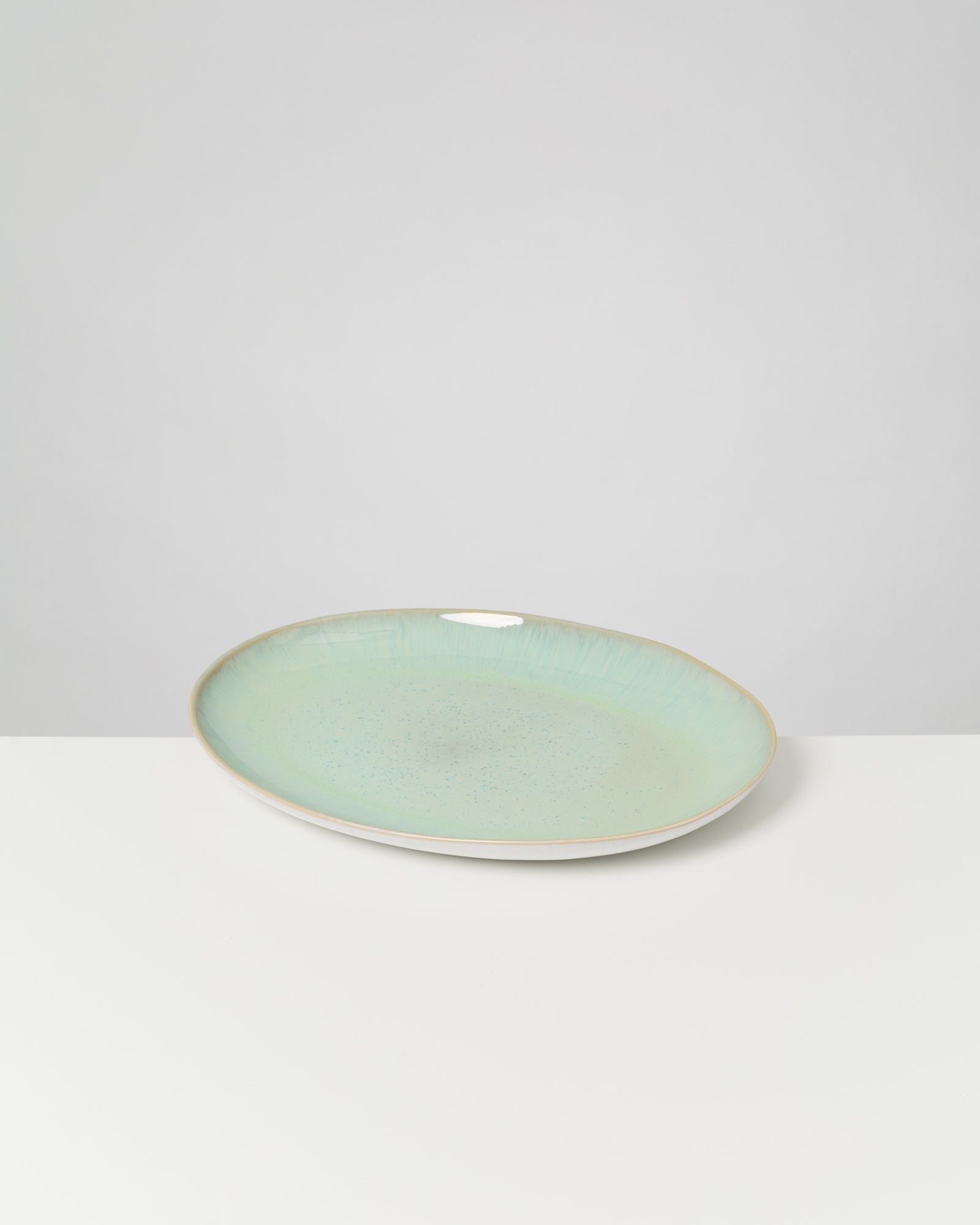 Ein hellgrüner, ovaler Keramikteller auf einem weißen Tisch vor einem grauen Hintergrund.