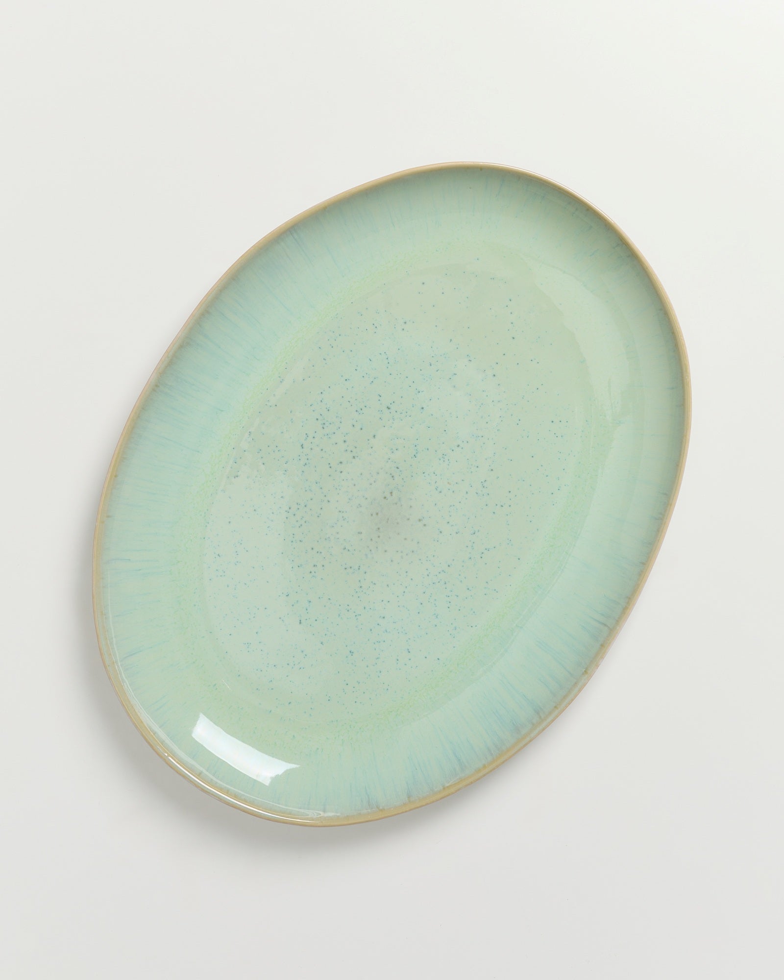 Grüner, ovaler Keramikteller mit blauen Sprenkeln auf einem weißen Hintergrund.
