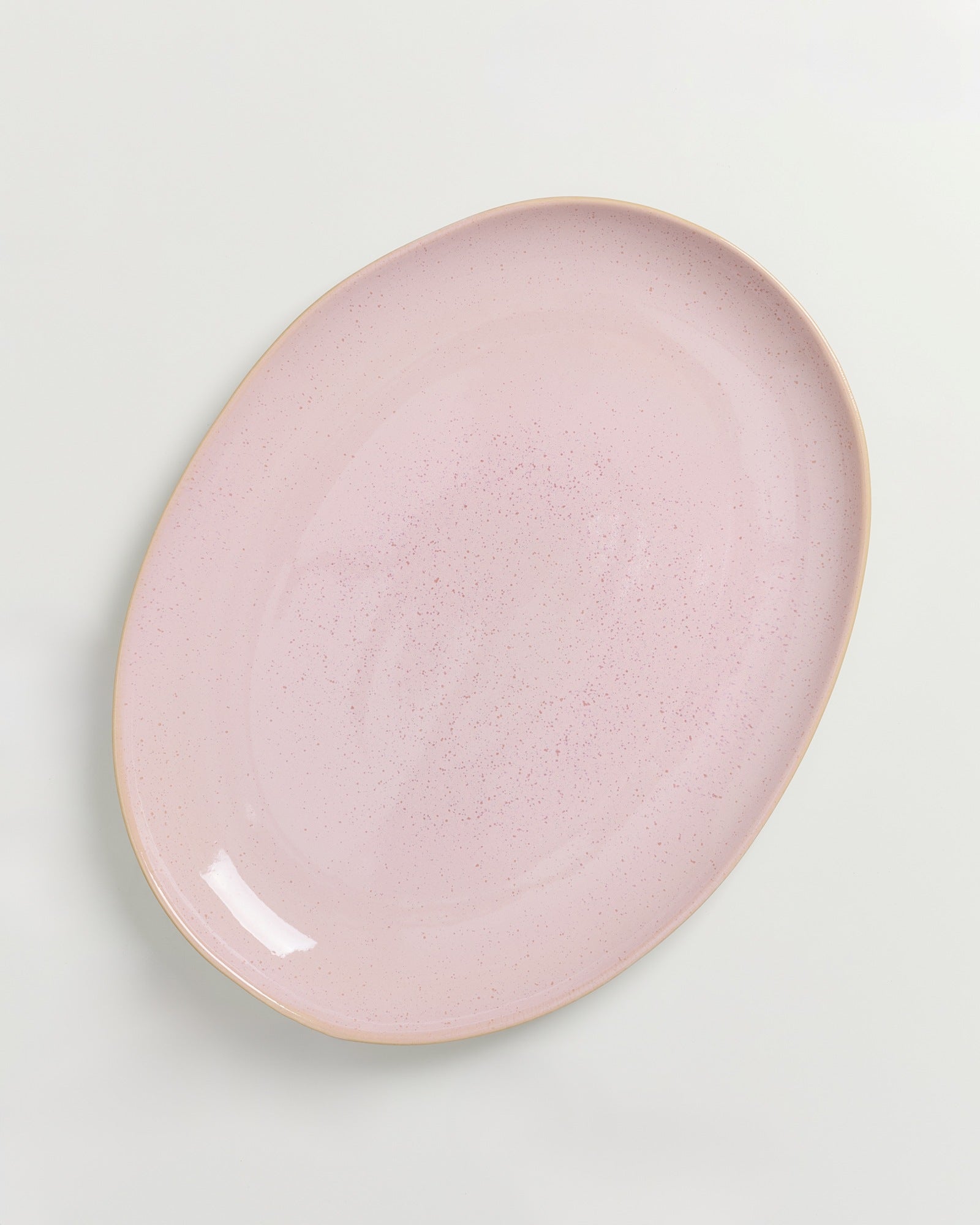 Ovaler, rosafarbener Teller mit leicht gesprenkeltem Muster auf hellgrauem Hintergrund.