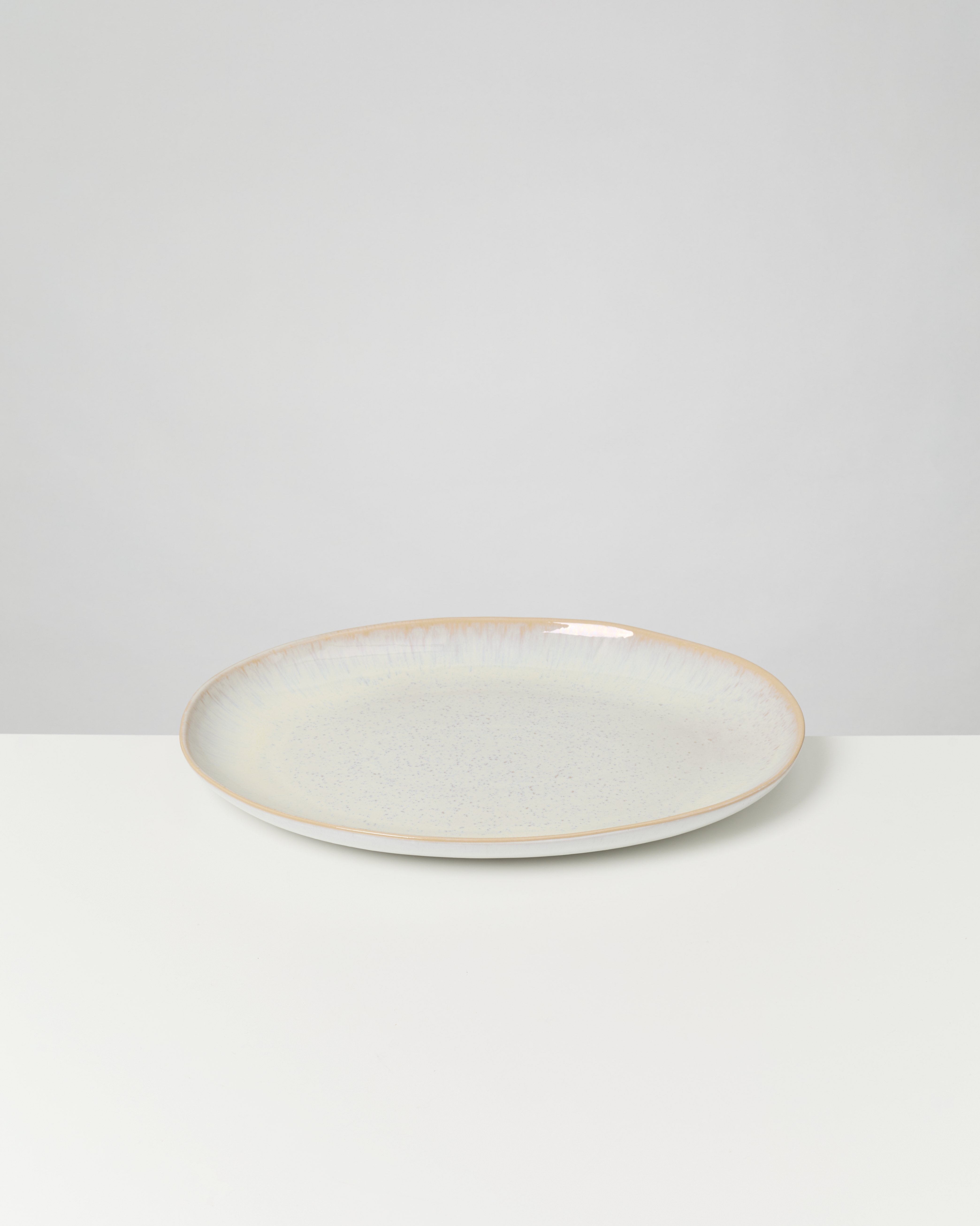 Ein weiß-grauer Keramikteller mit leicht bräunlichem Rand steht auf einem weißen Tisch vor einem hellgrauen Hintergrund.