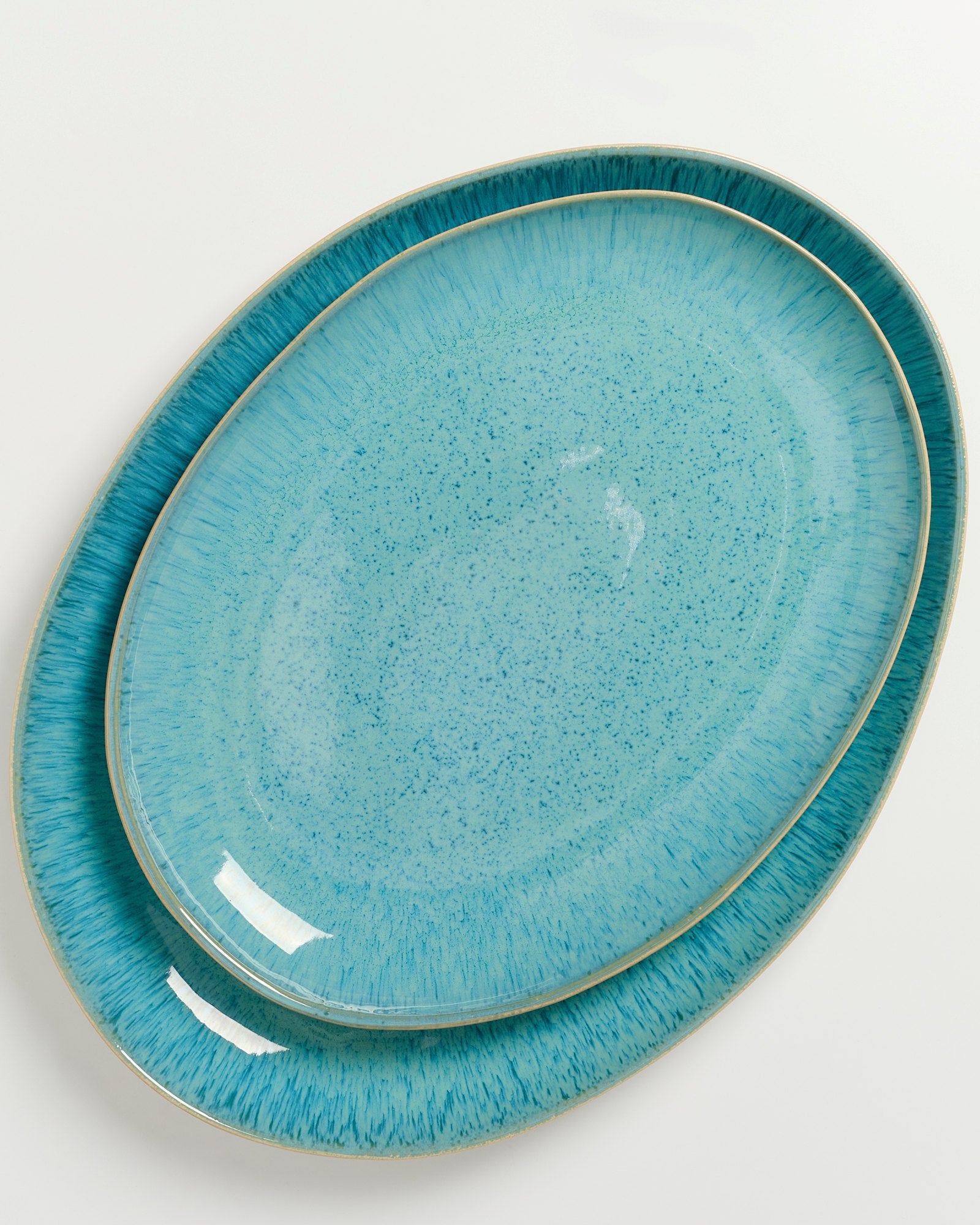 Zwei ovale, türkisfarbene Teller mit einer texturierten Oberfläche und einem dezenten Muster auf hellem Hintergrund.