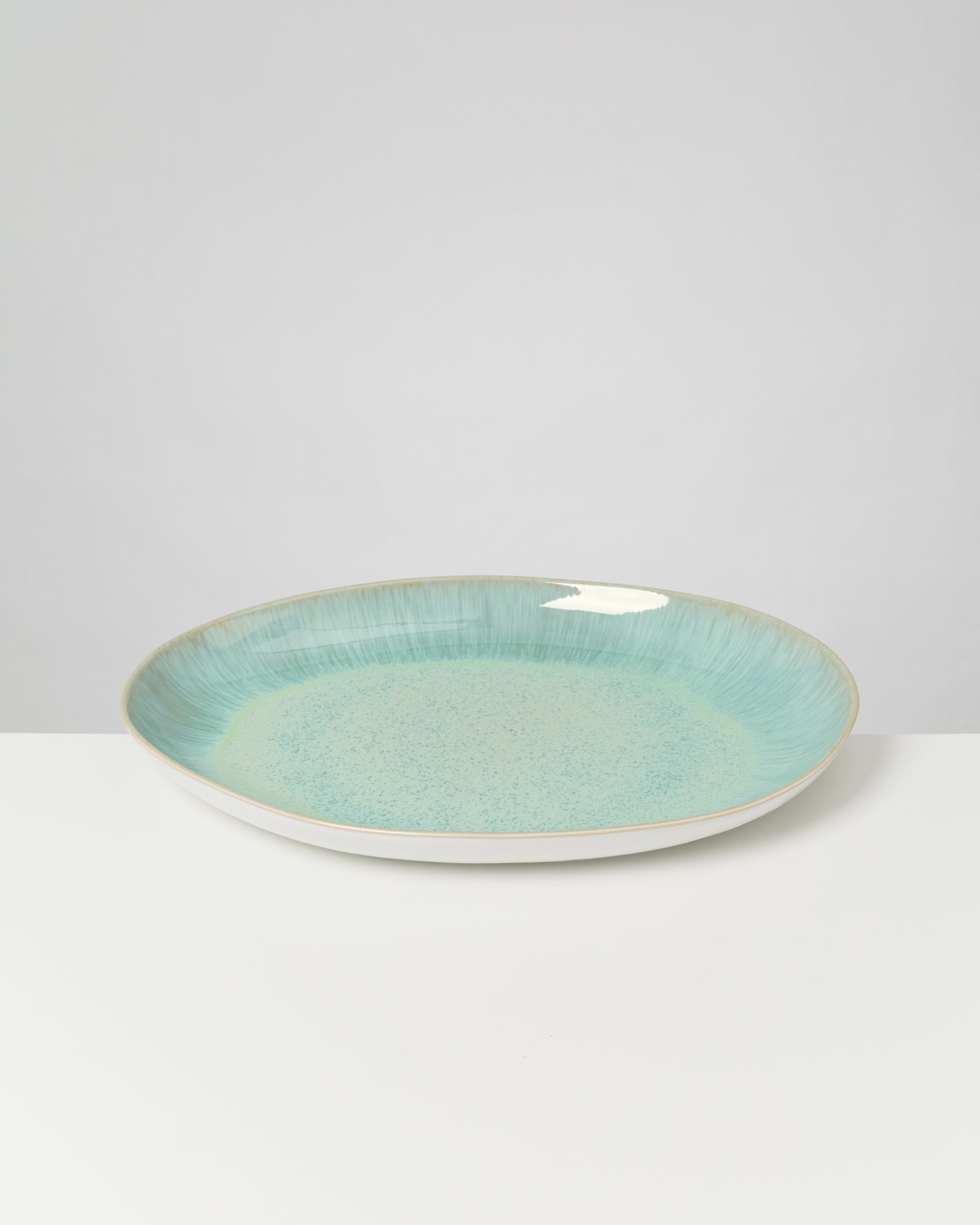 Großer, flacher Keramikteller mit einem blauen und grünen Verlauf auf einer weißen Oberfläche vor grauem Hintergrund.