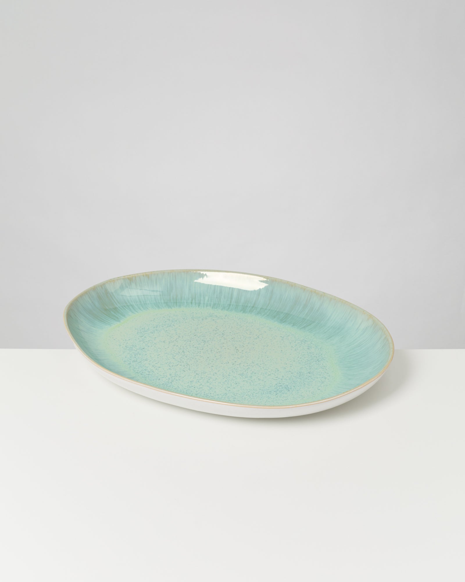 Ovaler Teller mit türkisfarbenem Muster auf einem weißen Untergrund.