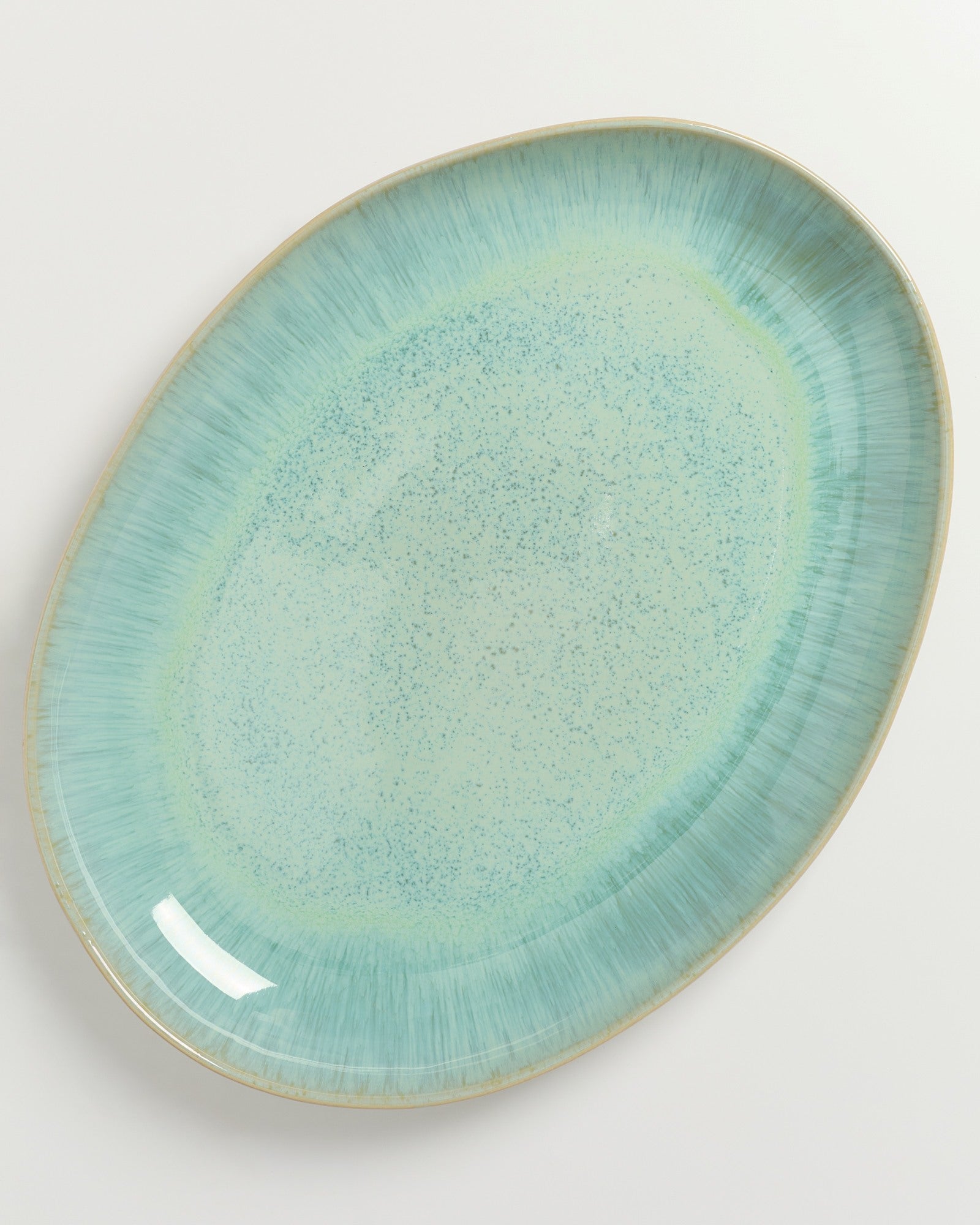 Ovaler Teller in Türkis- und Blautönen mit gesprenkeltem Muster auf weißem Hintergrund.
