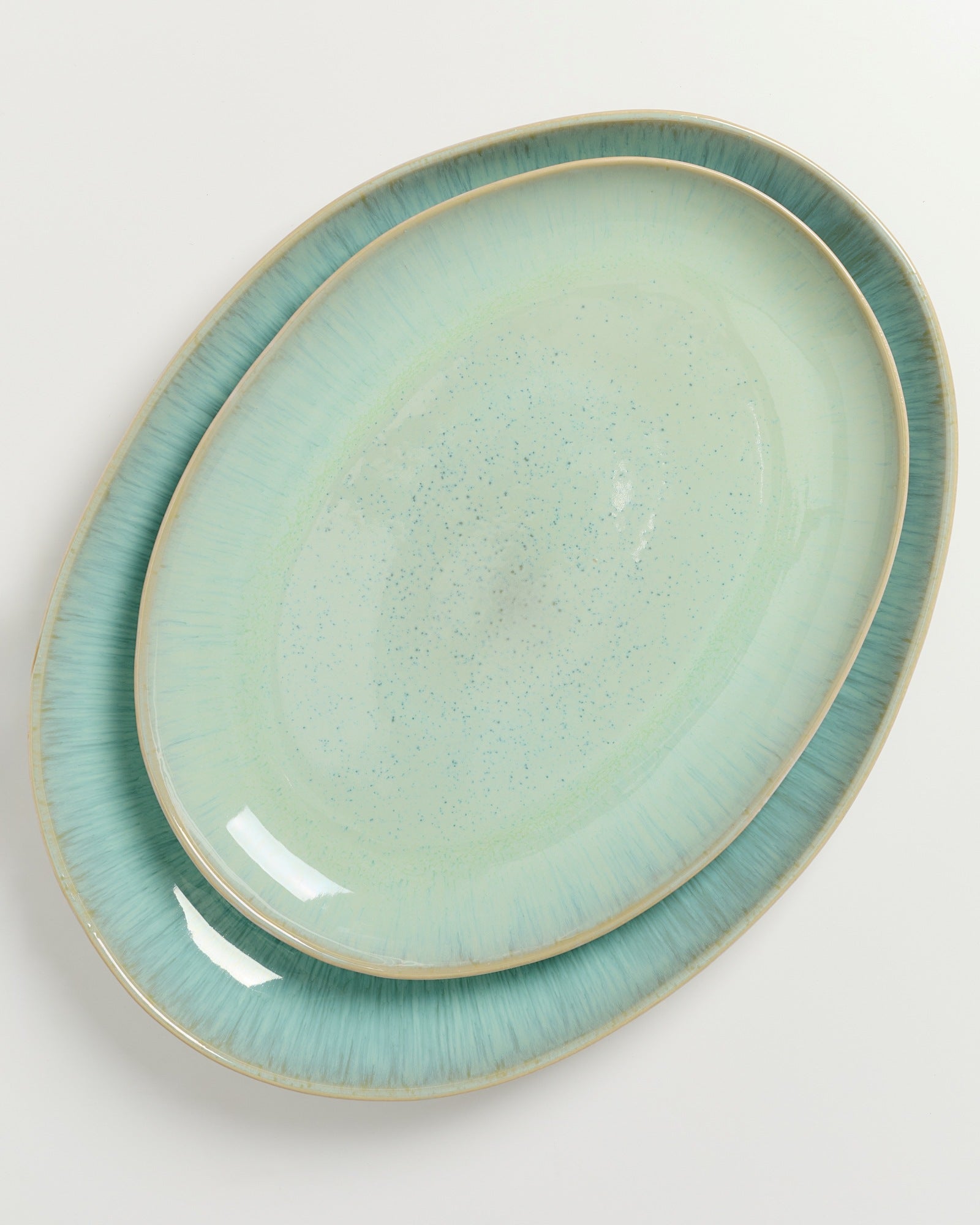 Zwei übereinanderliegende ovale Keramikteller in verschiedenen Blautönen mit gesprenkeltem Muster auf einem weißen Hintergrund.