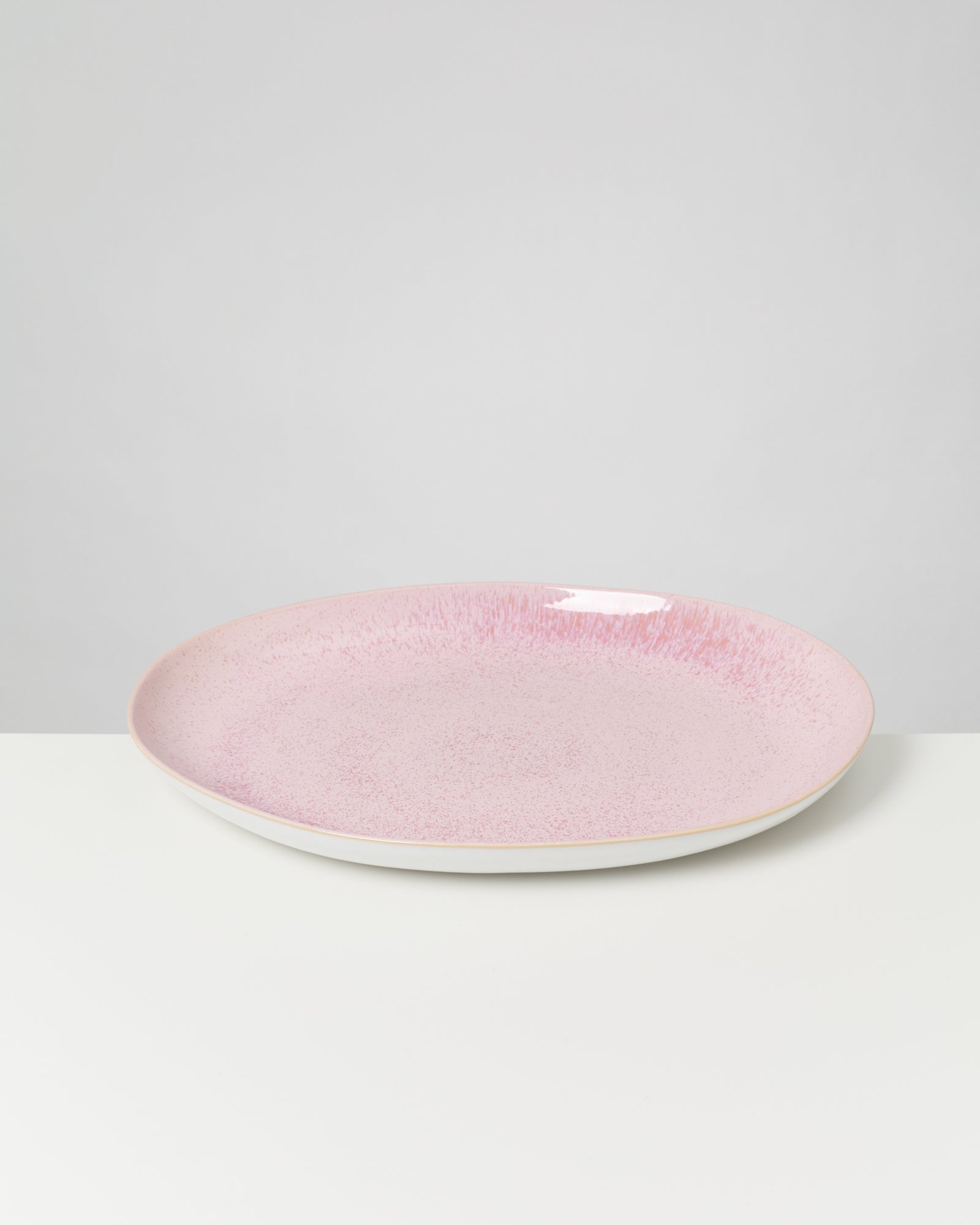 Ein rosa Keramikteller mit gesprenkelter Textur steht auf einem weißen Tisch vor einem neutralen Hintergrund.