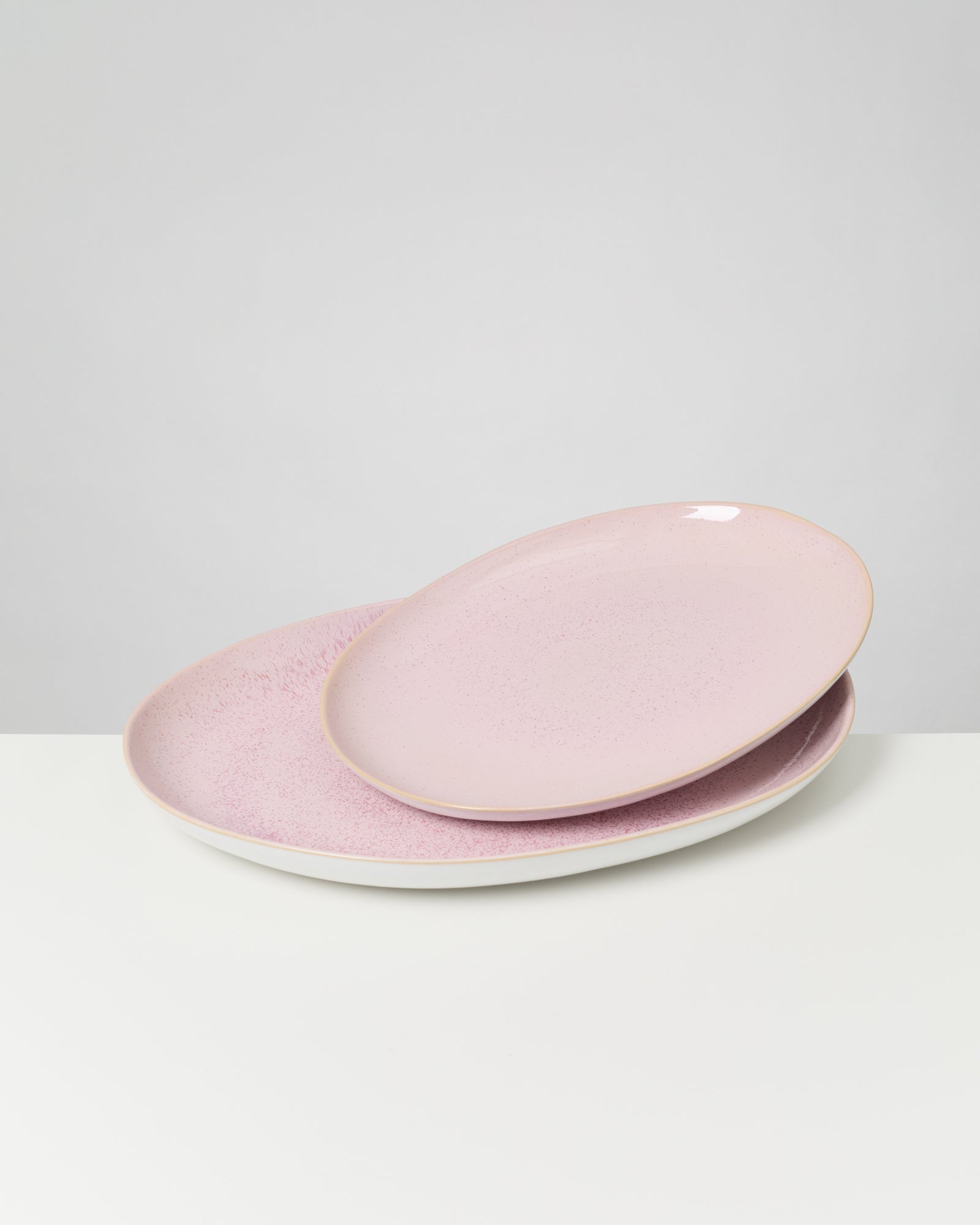 Zwei rosa ovale Teller stehen aufeinander auf einer weißen Oberfläche vor neutralem Hintergrund.