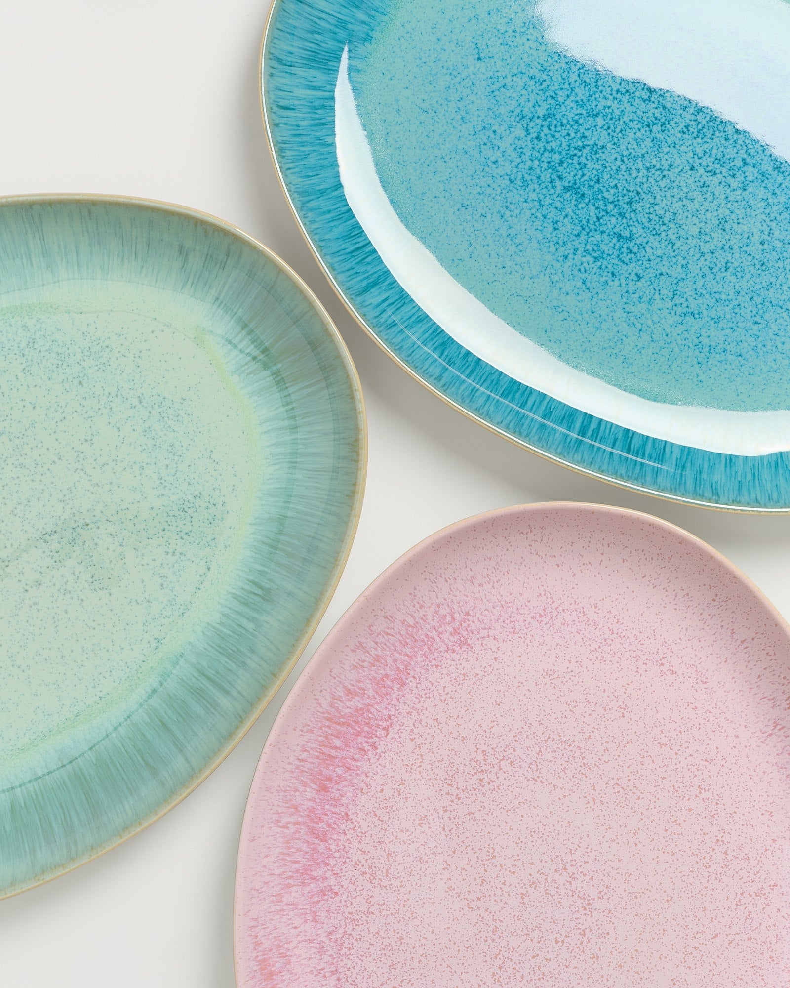 Drei ovale Teller in Türkis, Grün und Rosa mit gesprenkeltem Muster auf einer weißen Oberfläche.