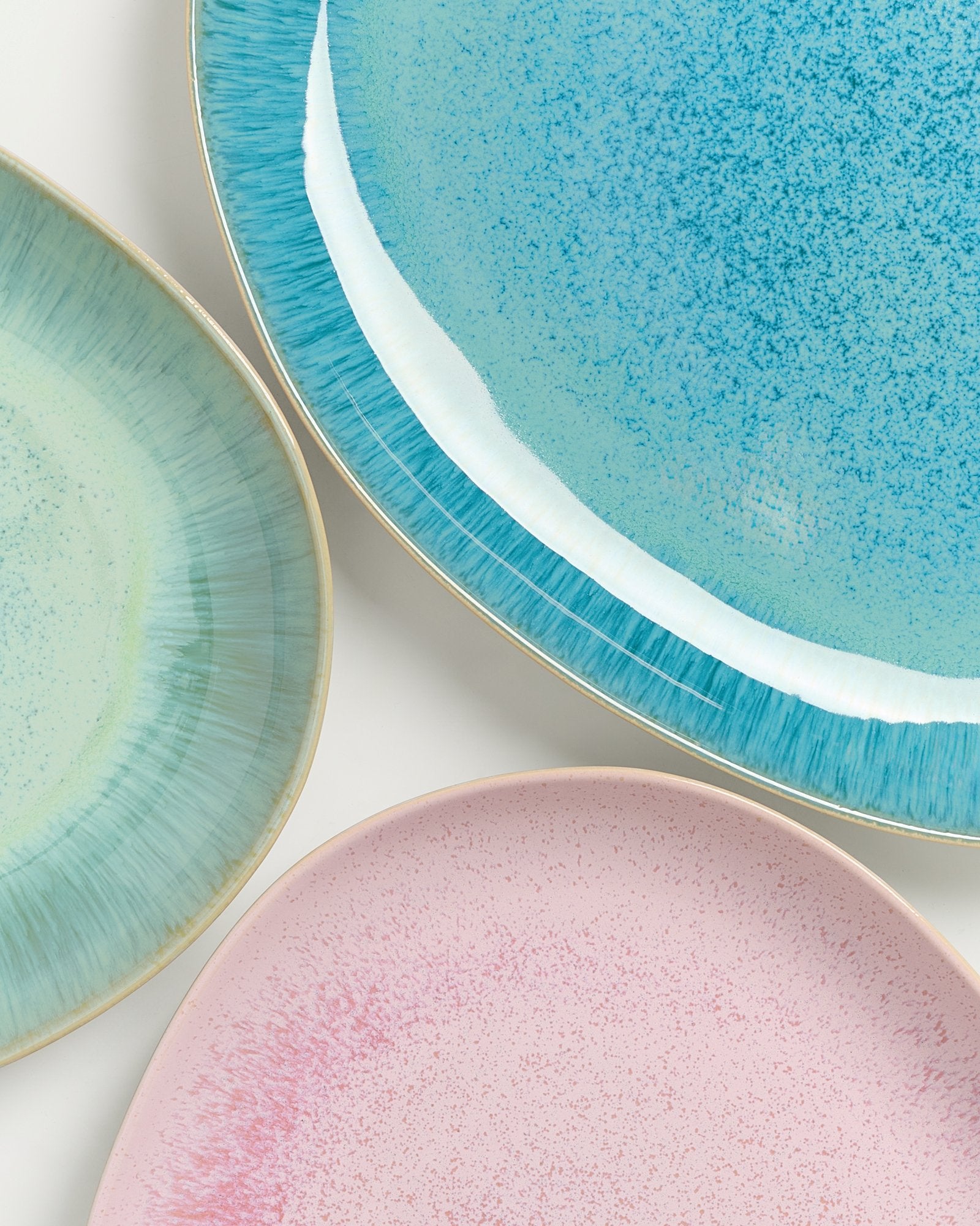 Drei verschiedenfarbige Teller in Blau, Grün und Rosa mit gesprenkeltem Muster auf einem weißen Hintergrund.