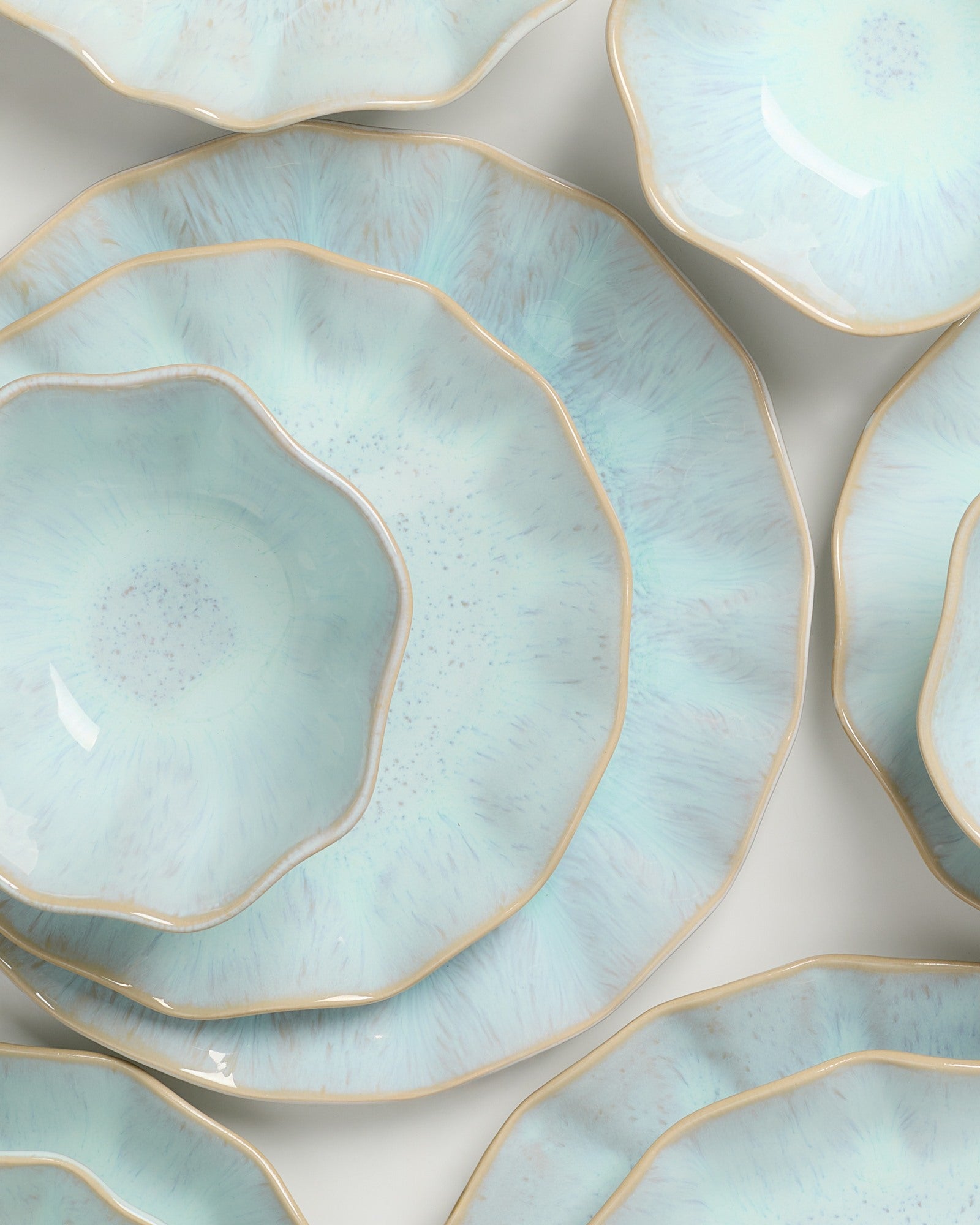 Mehrere türkisfarbene, wellenförmige Keramikteller mit goldenen Rändern liegen überlappend auf einer hellen Fläche.