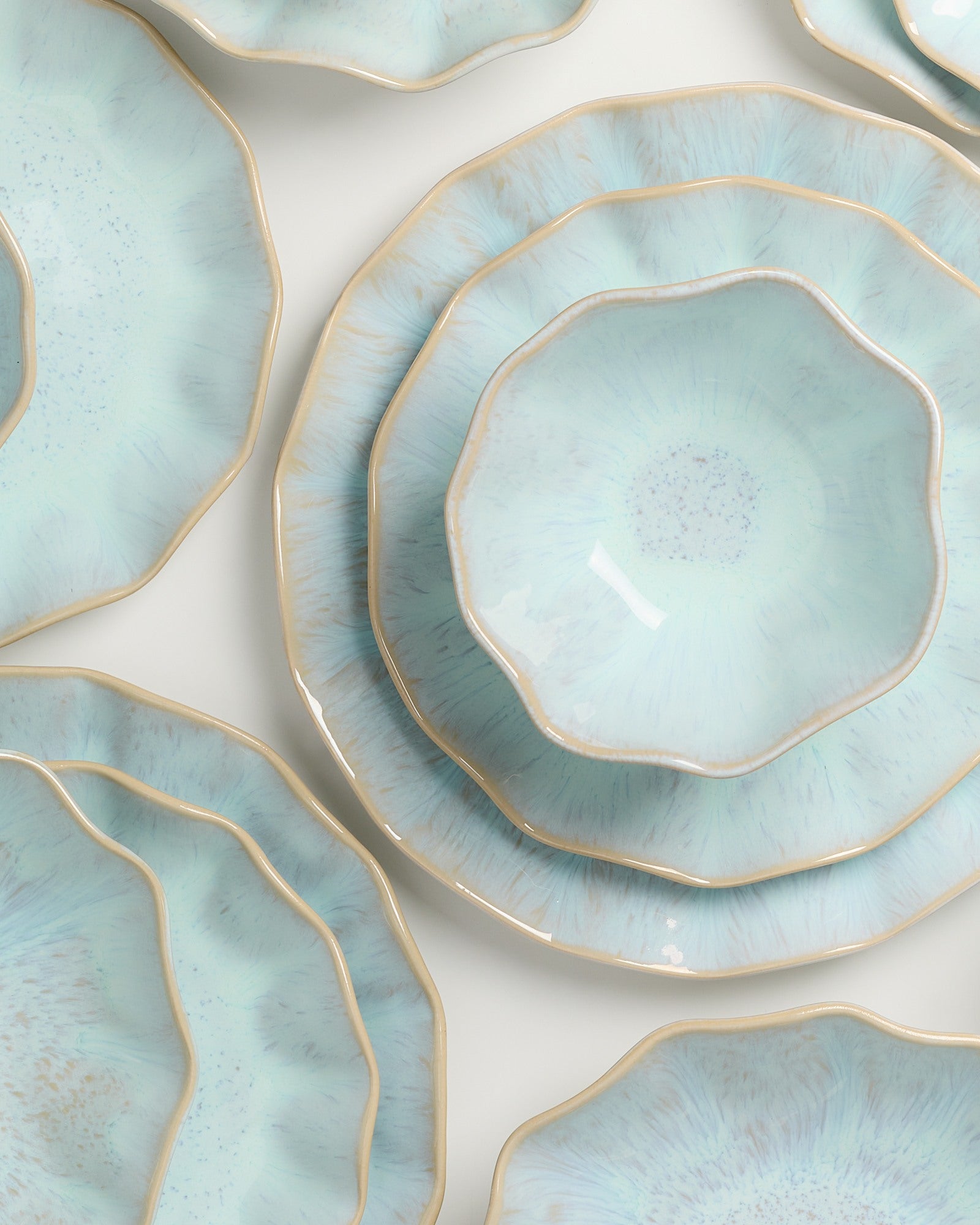 Mehrere türkisfarbene Teller mit unregelmäßigen Rändern und einem feinen, goldenen Rand sind übereinander gestapelt.