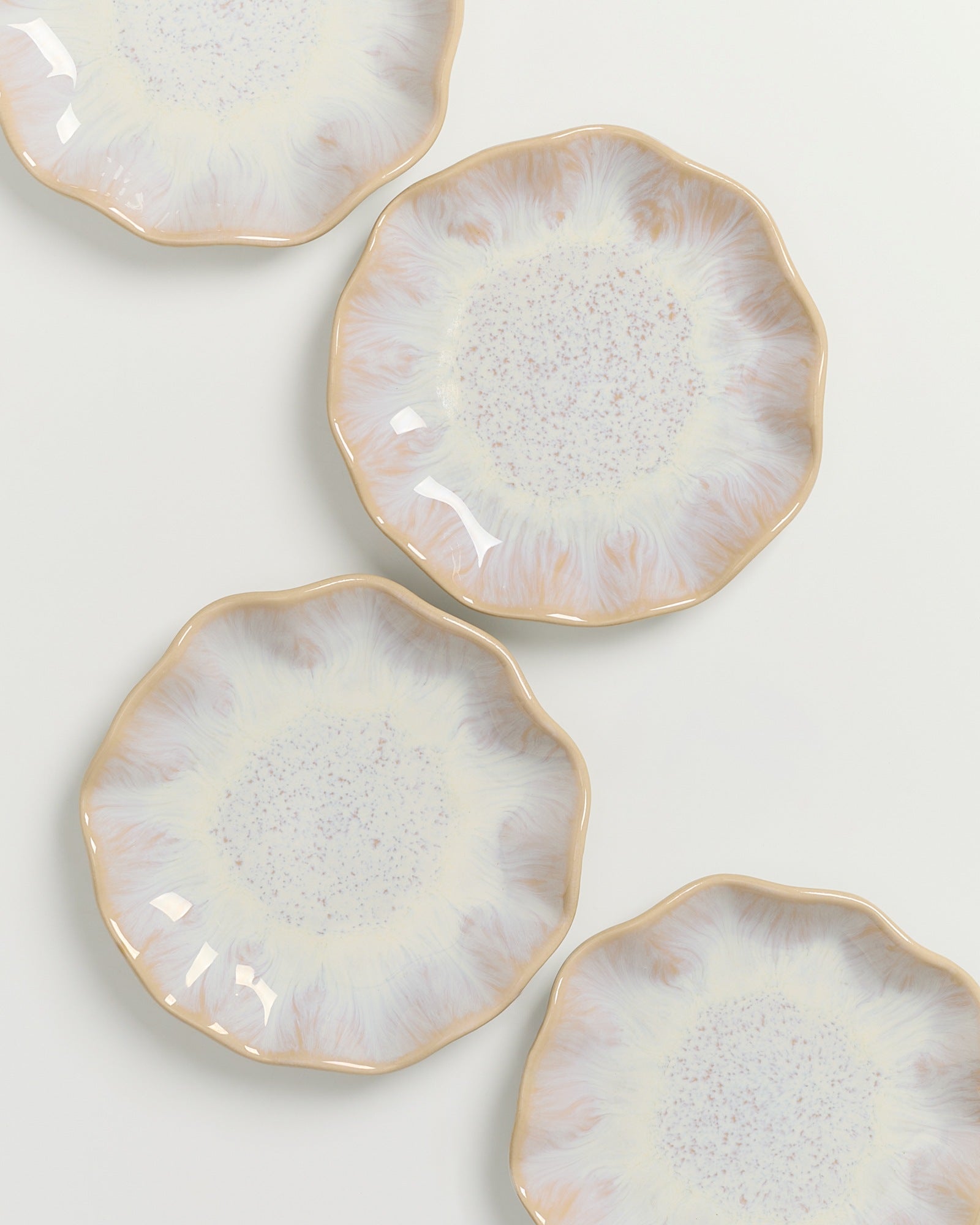 Vier dekorative, beige und cremefarbene Teller mit gewelltem Rand und gesprenkeltem Muster liegen auf weißem Hintergrund.