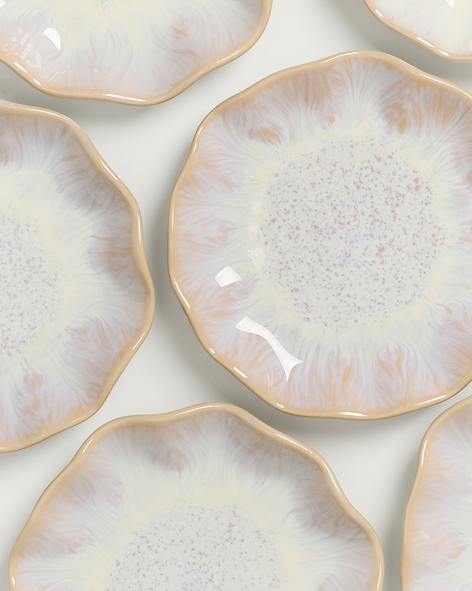 Nahaufnahme mehrerer dekorativer, blütenförmiger Teller mit einer Mischung aus pastellfarbenen und gesprenkelten Mustern.