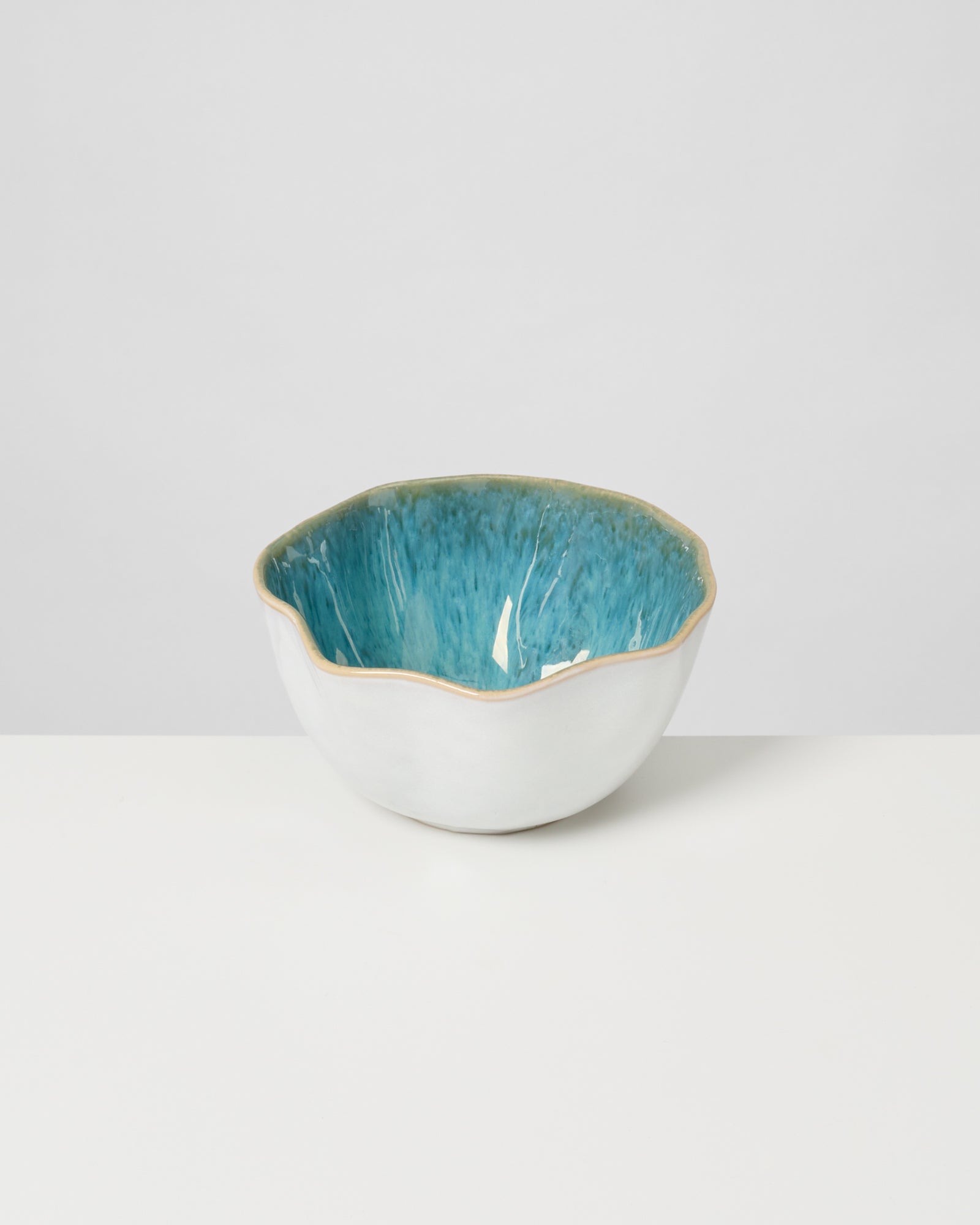 Weiße Keramikschale mit blauer, wellenförmiger Innenseite auf weißem Hintergrund.