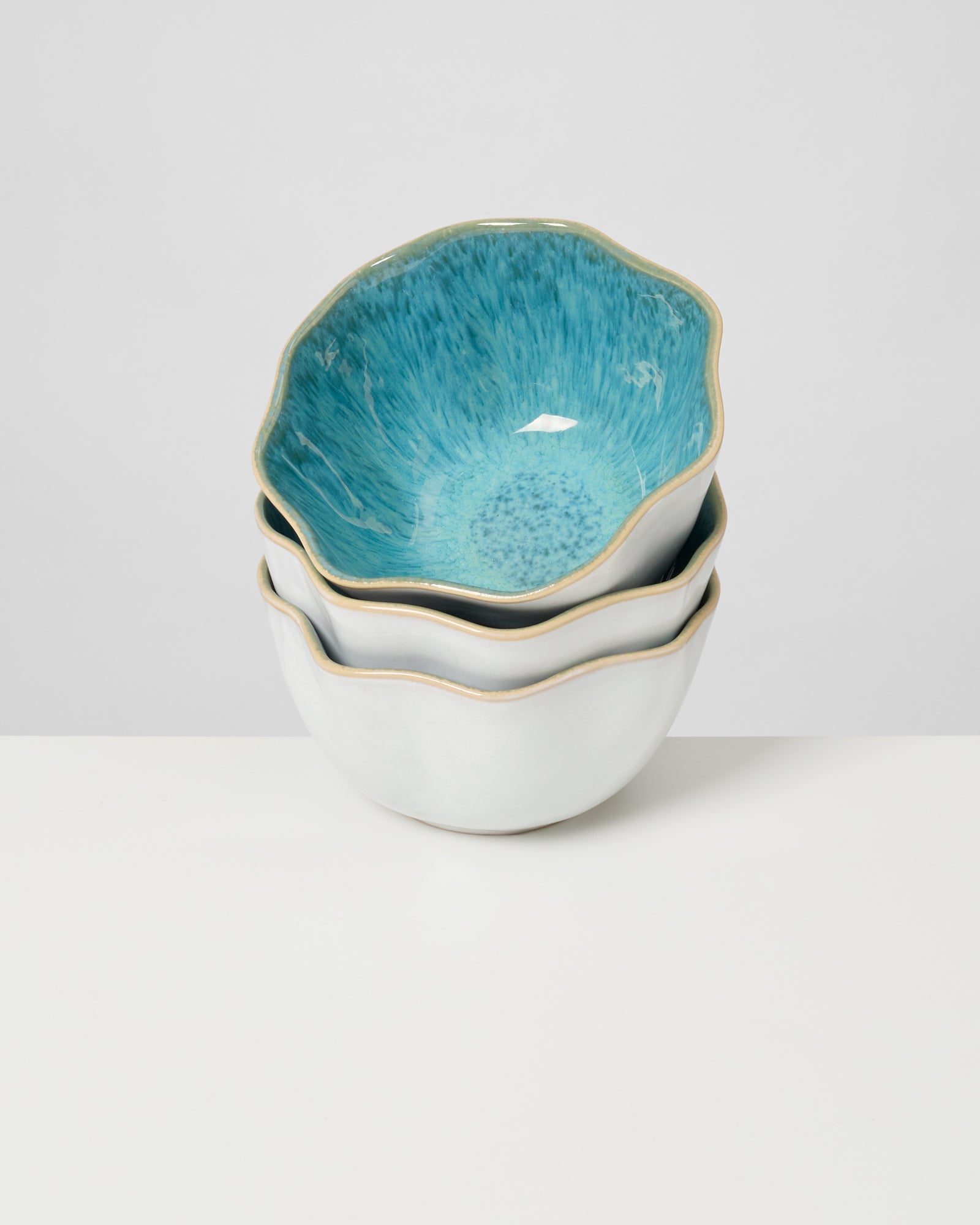 Drei gestapelte Keramikschalen mit blau-grüner Innenseite und weiß-goldenem Rand auf weißem Hintergrund.