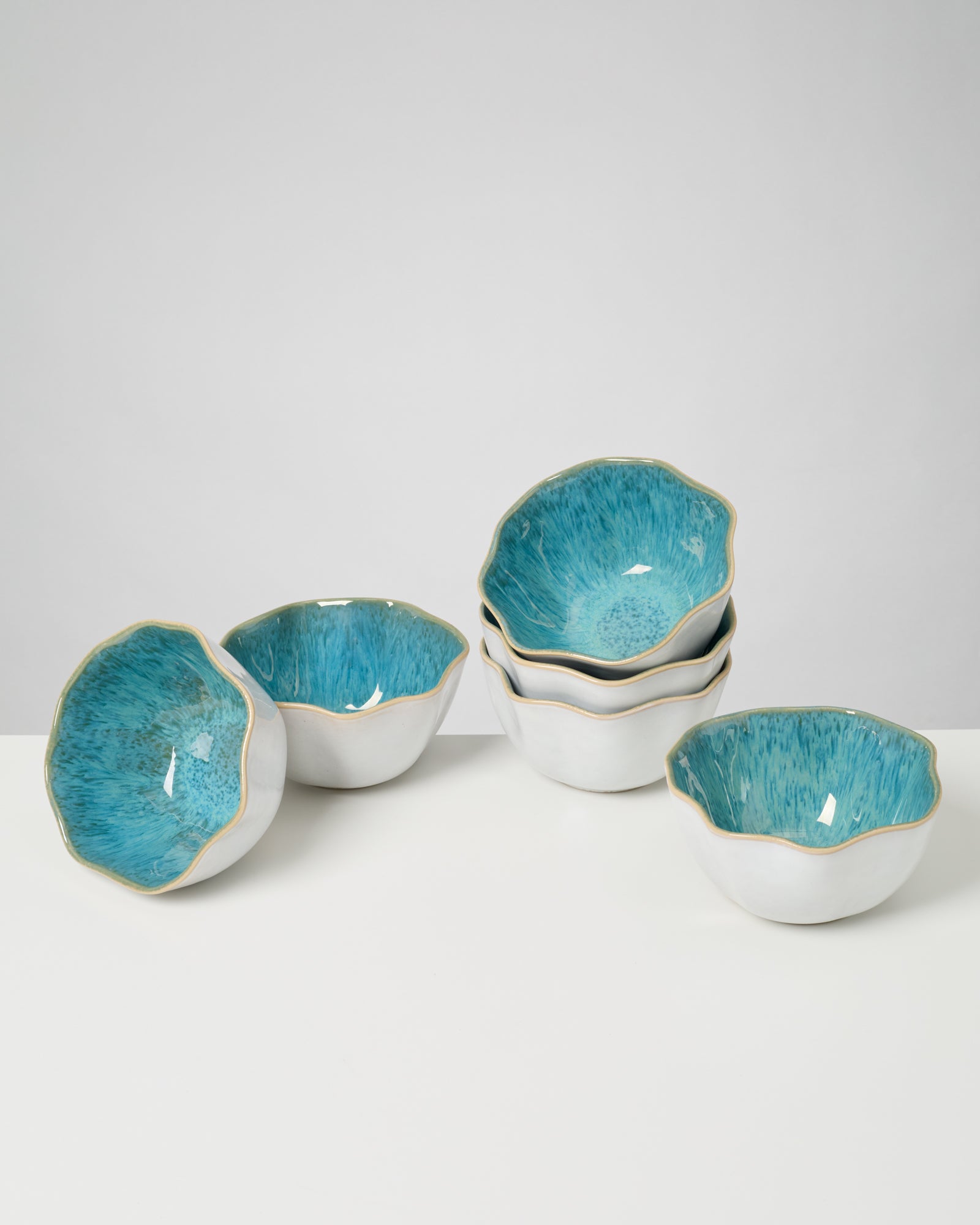 Sechs weiße Keramikschalen mit blauer Innenseite auf einem weißen Tisch.