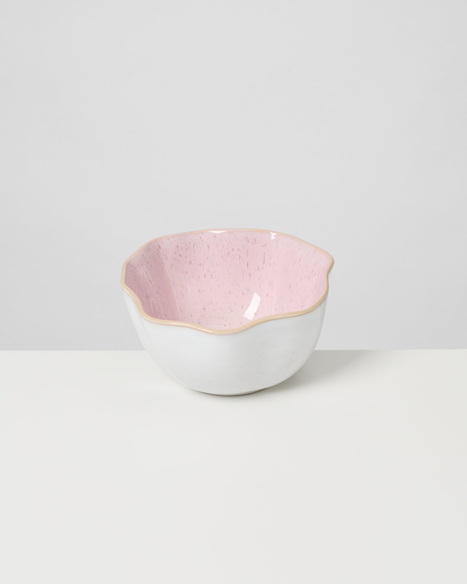 Weiße Schale mit rosanem, gewelltem Innenrand auf hellem Hintergrund.