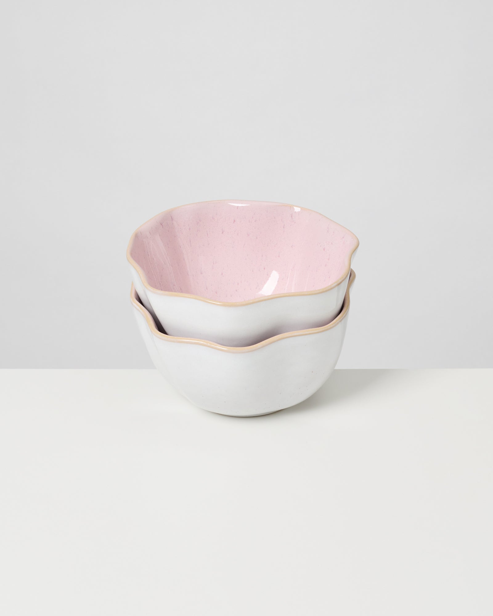 Zwei gestapelte Schalen mit rosa Innenfläche und welligem Rand auf weißem Hintergrund.